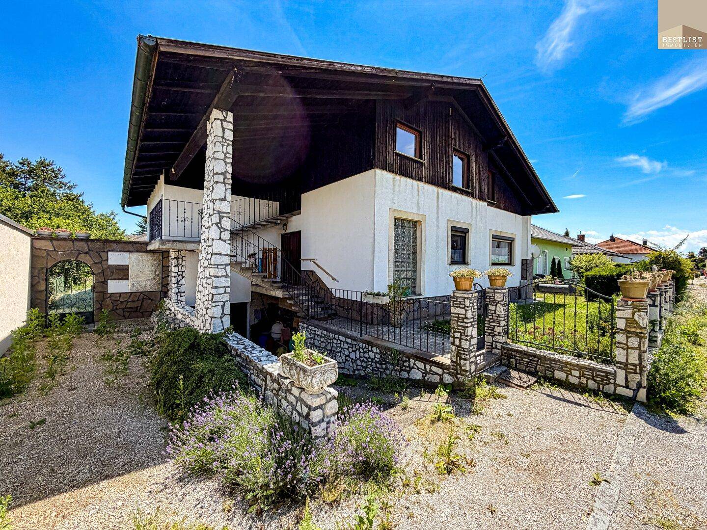 Traditionelles Haus mit Steinfassade, Balkon und gepflegtem Vorgartenbereich.