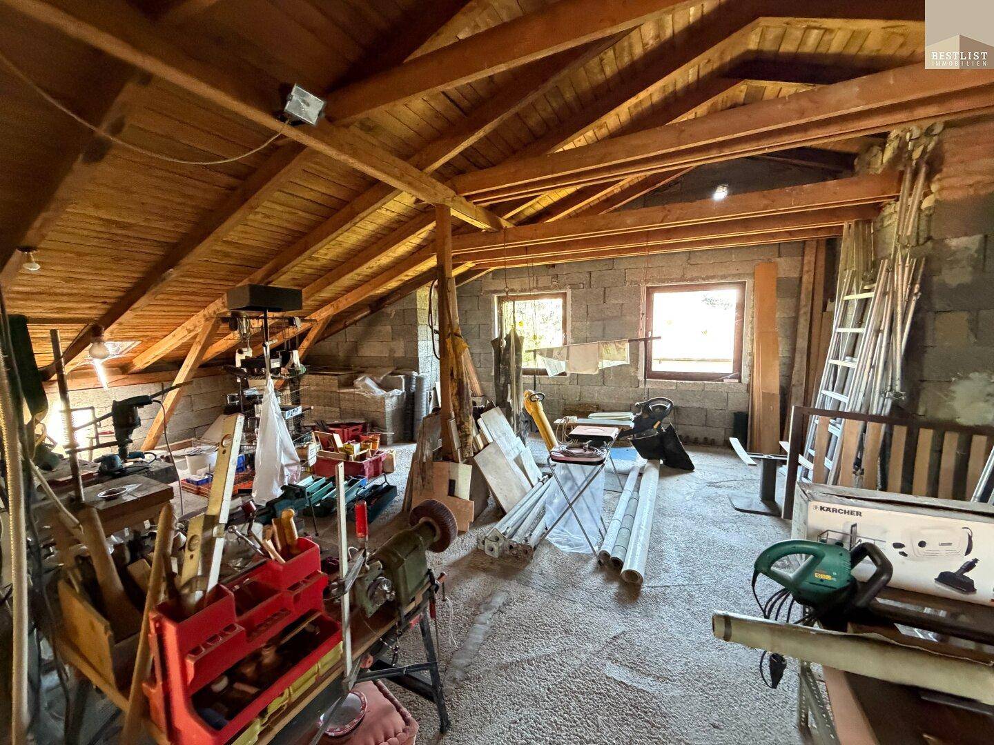 Geräumiger Dachboden mit sichtbaren Holzbalken, viel Stauraum und Fenstern für Tageslicht.