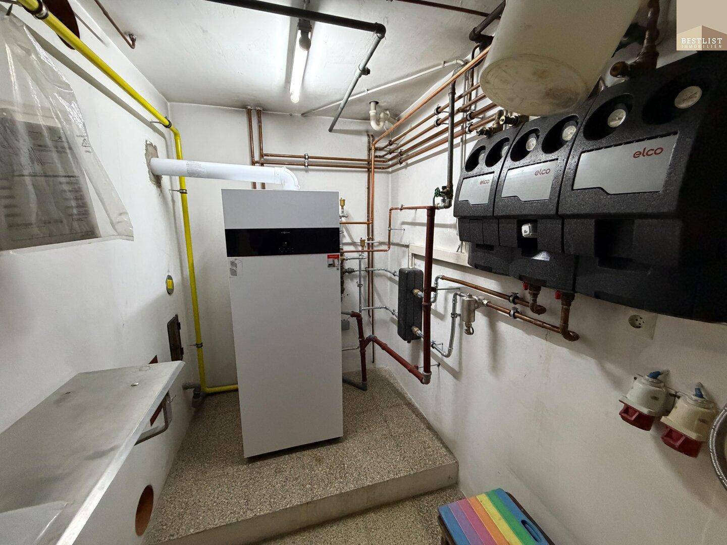 Heizungsraum mit moderner Heizungsanlage und Warmwasserspeicher im Kellerbereich.