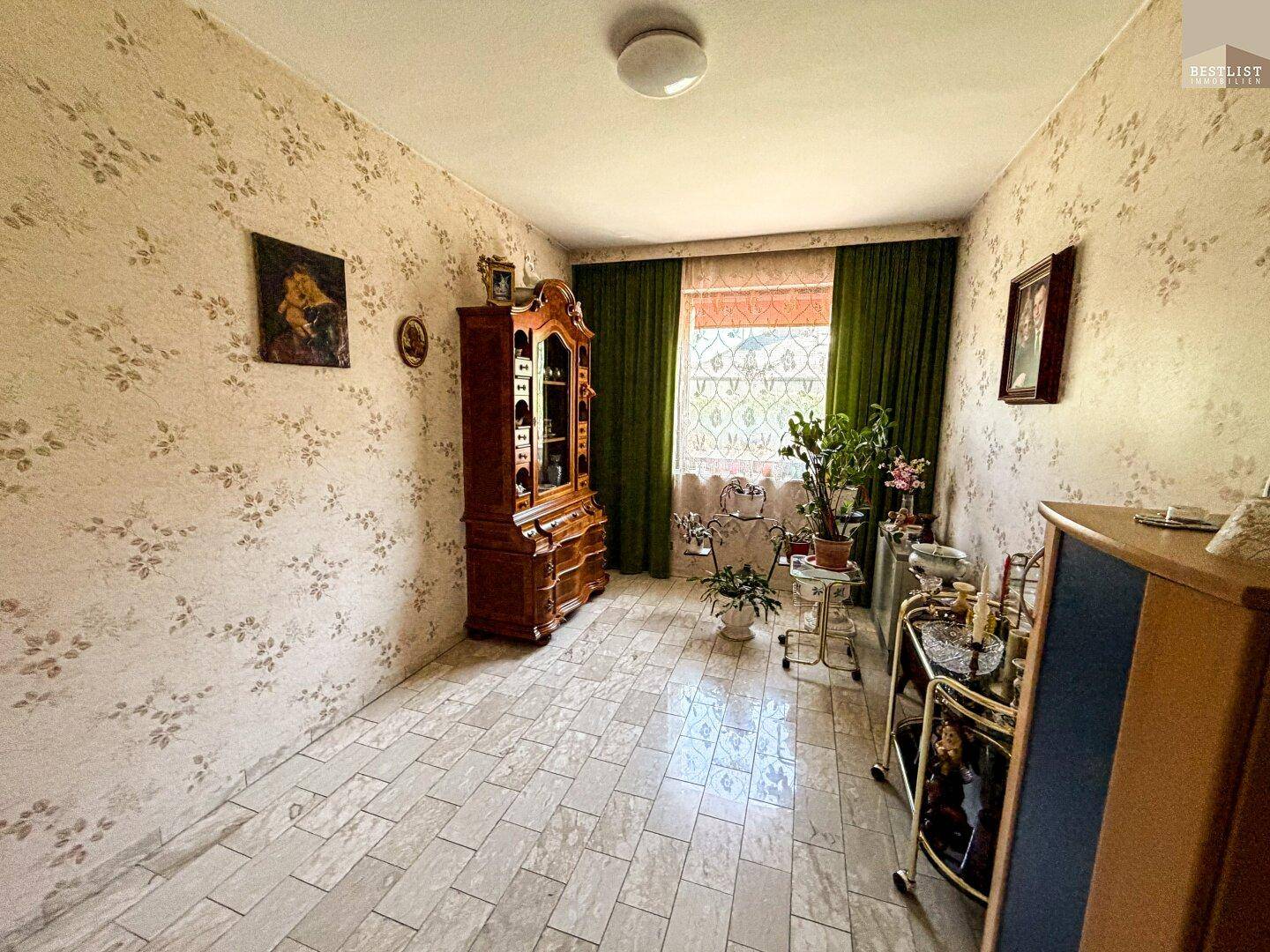 Gemütlicher Raum mit gemusterter Tapete, Fliesenboden und traditionellen Holzmöbeln.