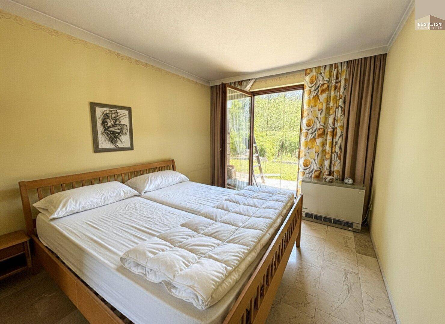 Helles Schlafzimmer mit Doppelbett, Fliesenboden und direktem Zugang zum Gartenbereich.