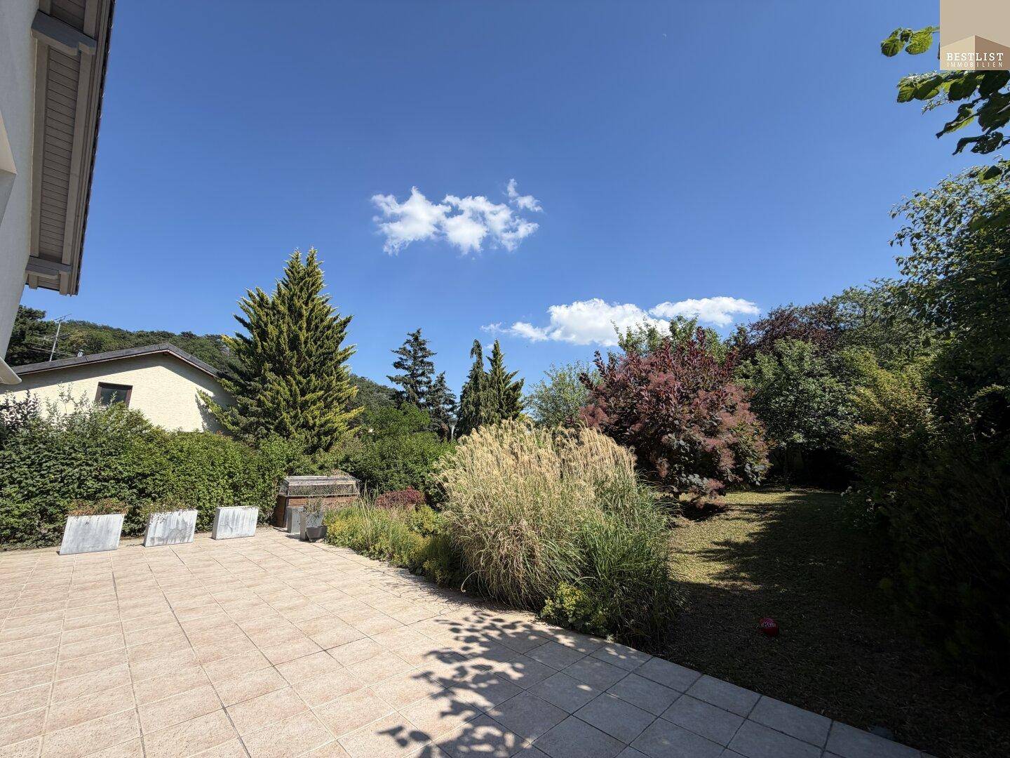 Geräumige Fliesenterrasse mit Blick auf den grünen Garten und die umliegende Landschaft.