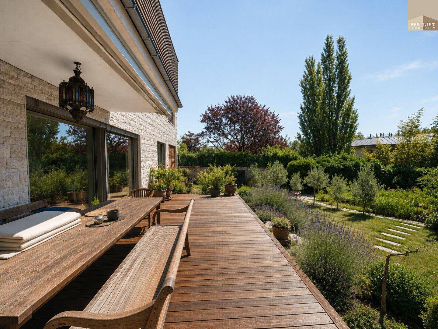 Große Holzterrasse mit Esstisch und Bänken, umgeben von einem gepflegten Garten.