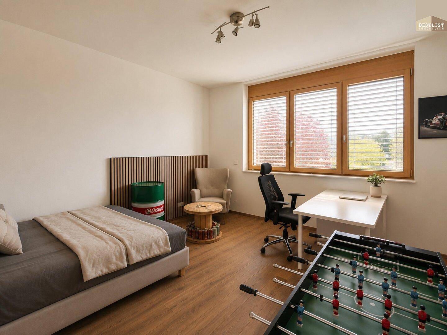 Jugendzimmer mit Holzboden, Schreibtisch und Blick ins Grüne durch große Fenster.