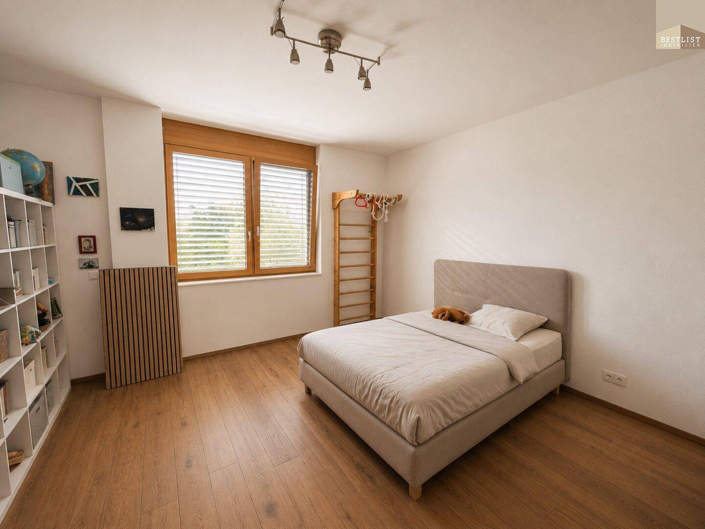 Helles Schlafzimmer mit Holzboden, großem Fenster und einfacher, moderner Einrichtung.