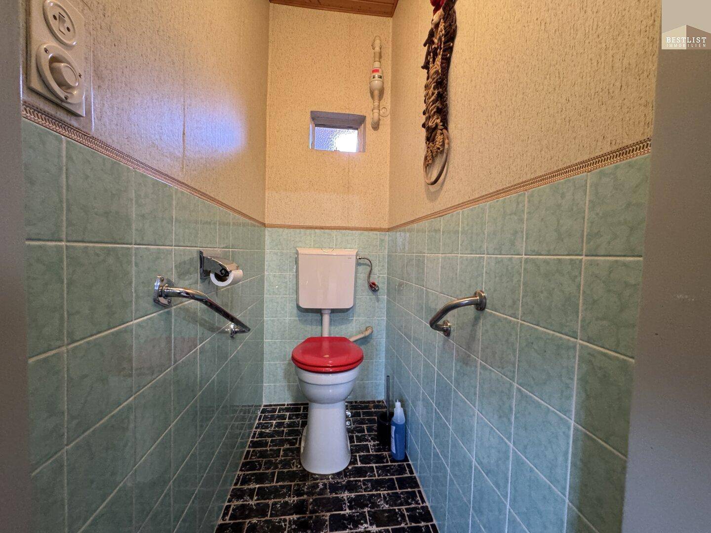 Separate Toilette mit hellgrünen Fliesen, Haltegriffen und einem kleinen Fenster.