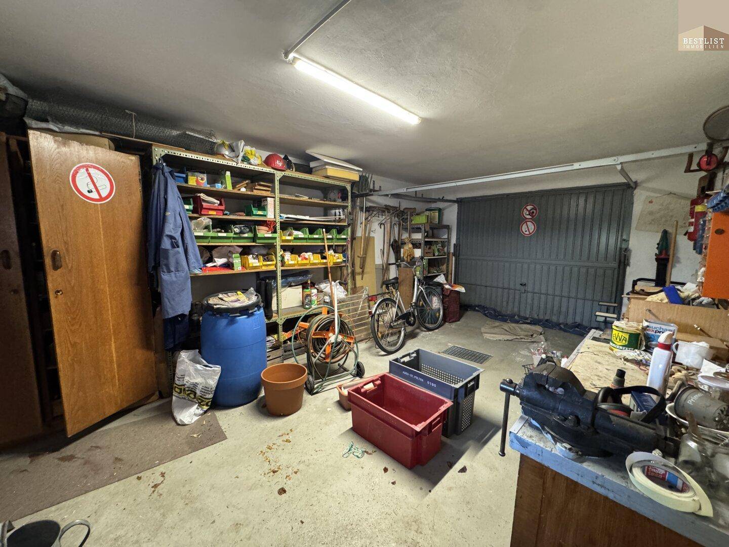 Geräumige Garage mit Rolltor, Regalen und Abstellmöglichkeiten für Fahrräder und Werkzeuge.