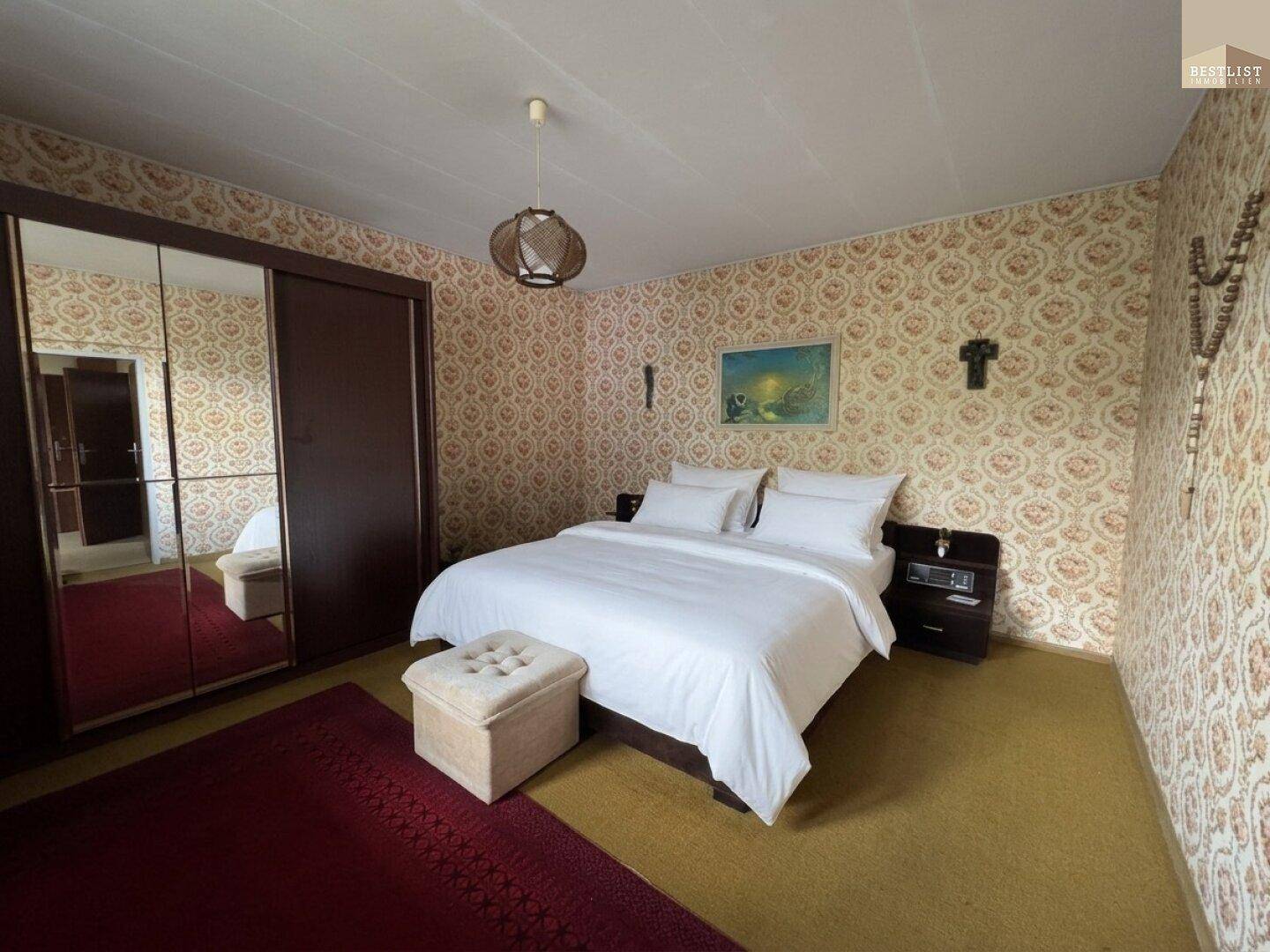 Schlafzimmer mit Doppelbett, Spiegelschrank und gemusterter Tapete im Vintage-Stil.
