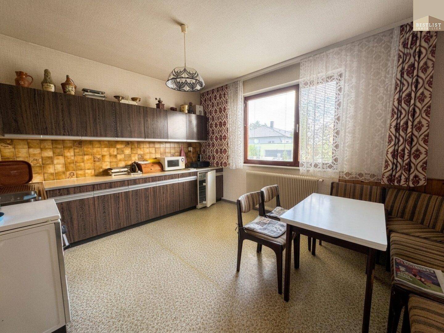 Traditionelle Küche mit dunklen Holzschränken, Essbereich und einem Fenster mit Blick nach draußen.