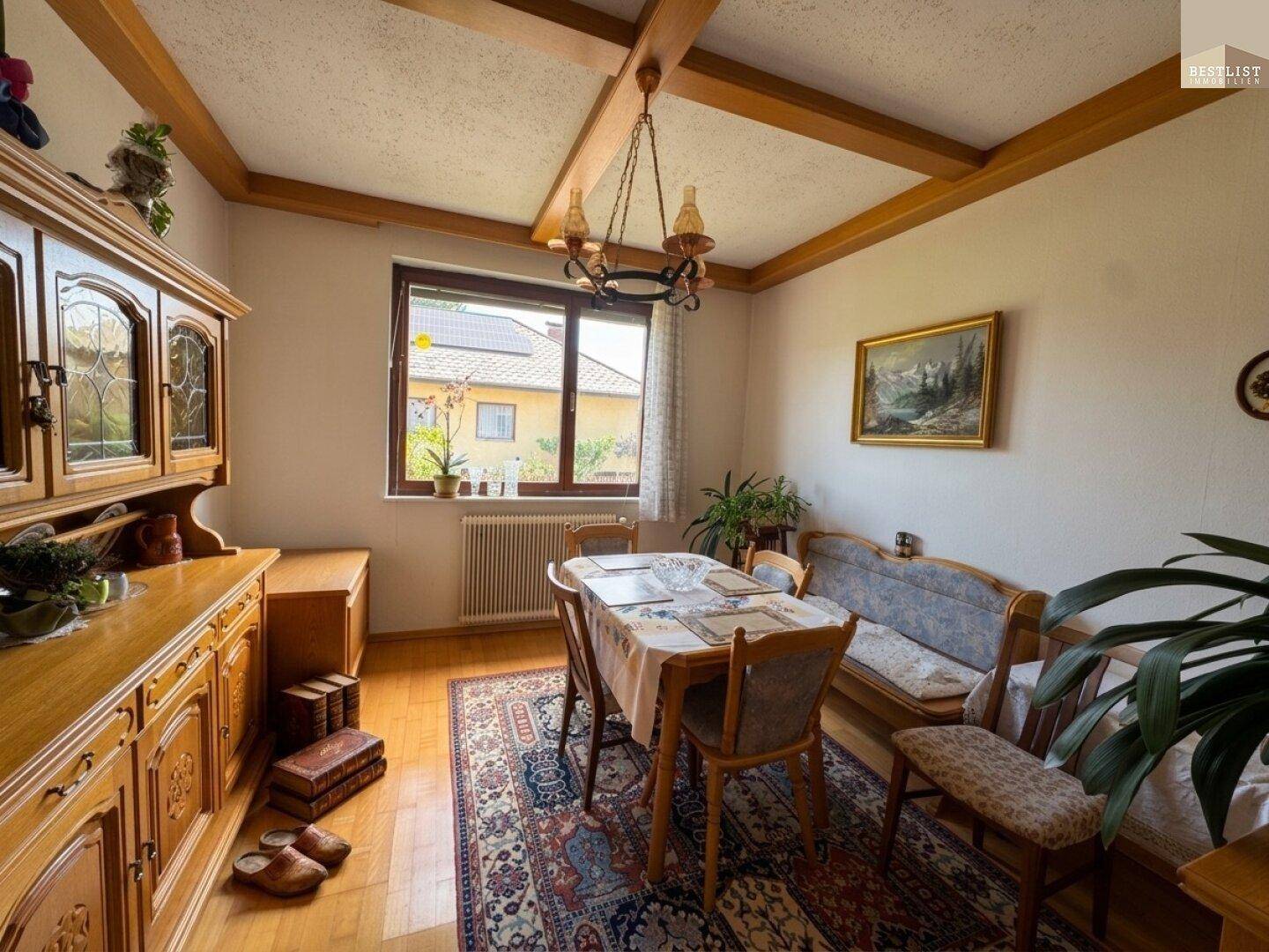Esszimmer mit Holzbalkendecke, traditionellen Möbeln und einem Fenster mit Blick ins Grüne.