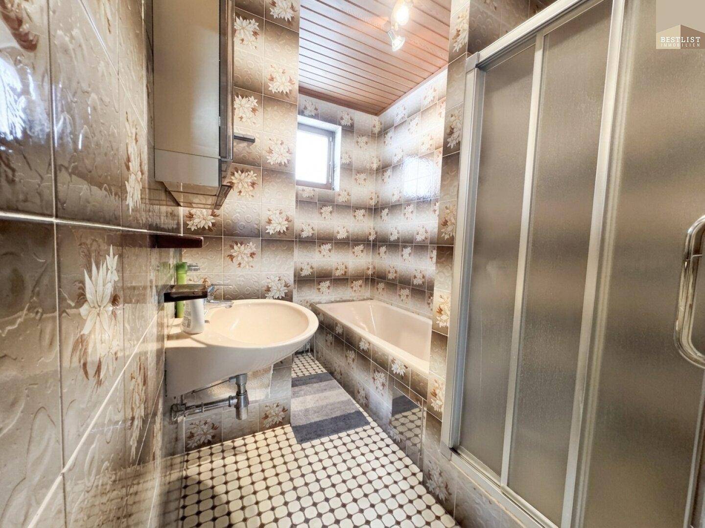 Badezimmer mit Badewanne, Duschkabine und gemusterten Fliesen im Retro-Design.