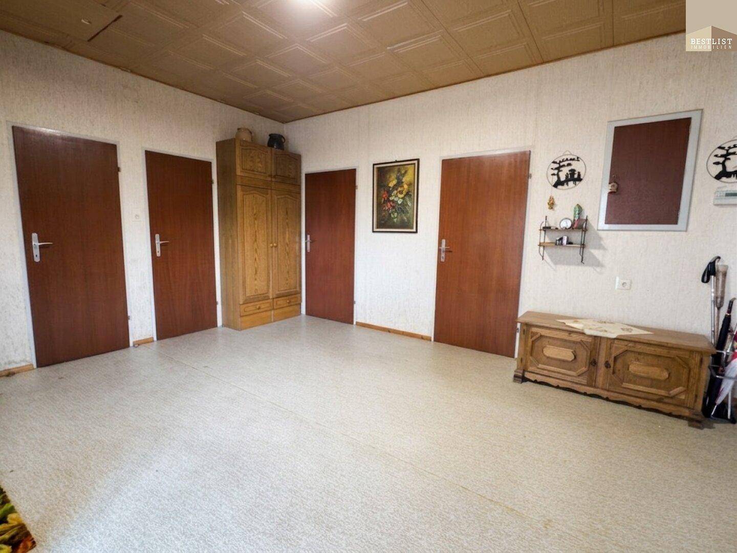 Geräumiger Flur mit mehreren Holztüren, einem Schrank und einfacher Deckenverkleidung.