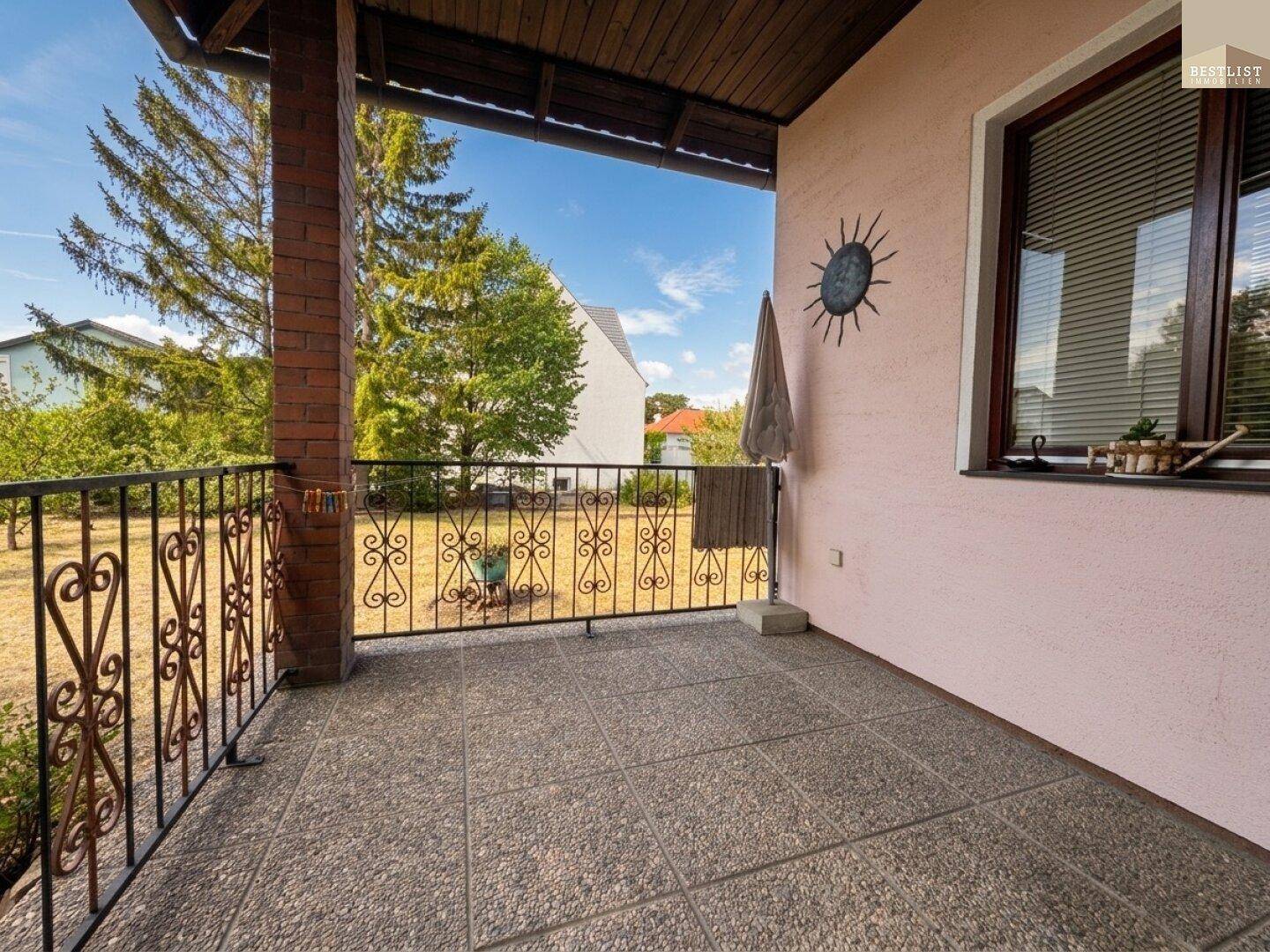 Überdachter Balkon mit Fliesenboden und schmiedeeisernem Geländer, bietet einen Blick ins Grüne.