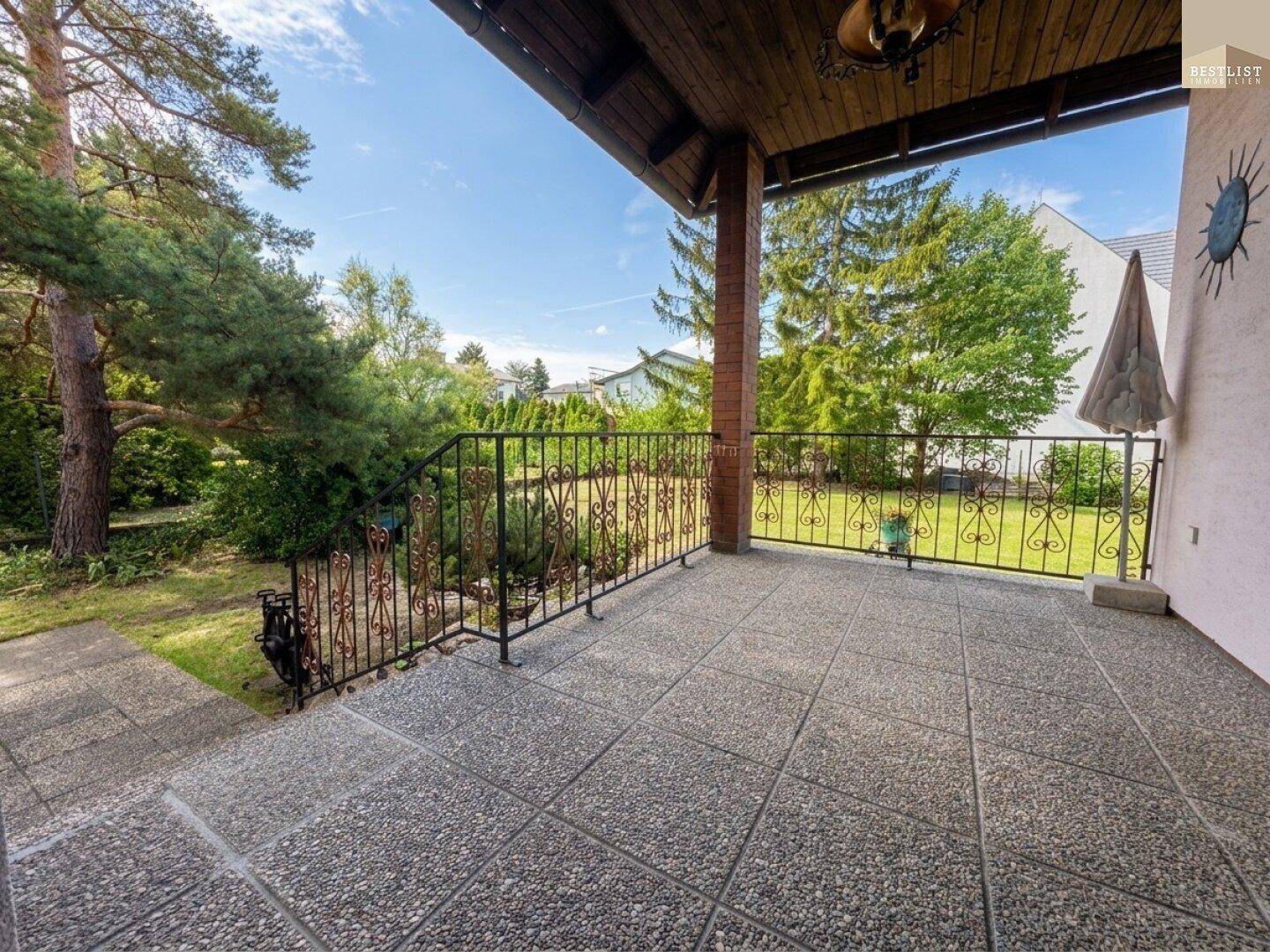Geräumiger überdachter Balkon mit Fliesenboden und Blick auf den umliegenden Gartenbereich.