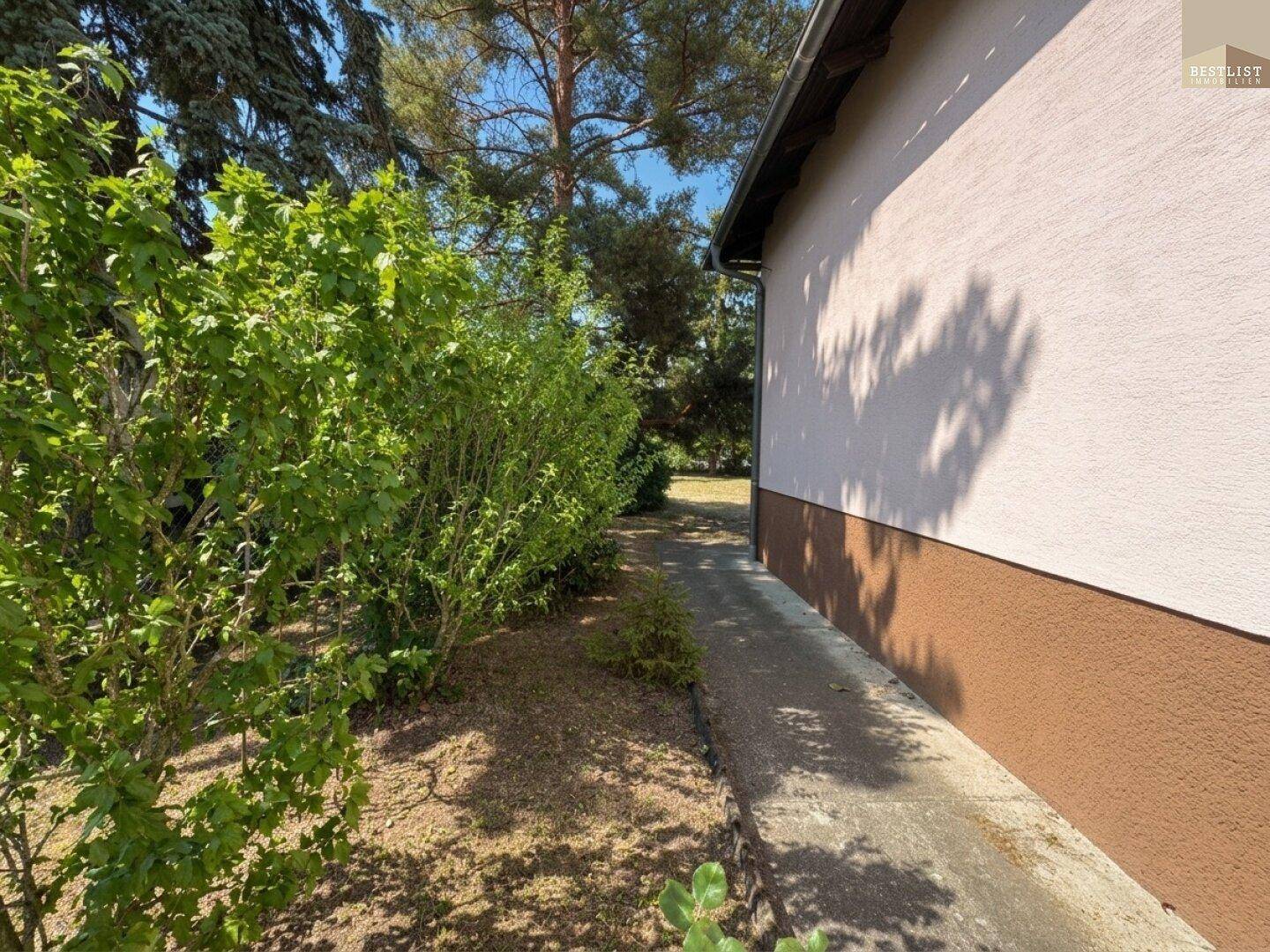 Seitenansicht des Hauses mit einem schmalen Gartenweg und üppigen Büschen entlang der Fassade.