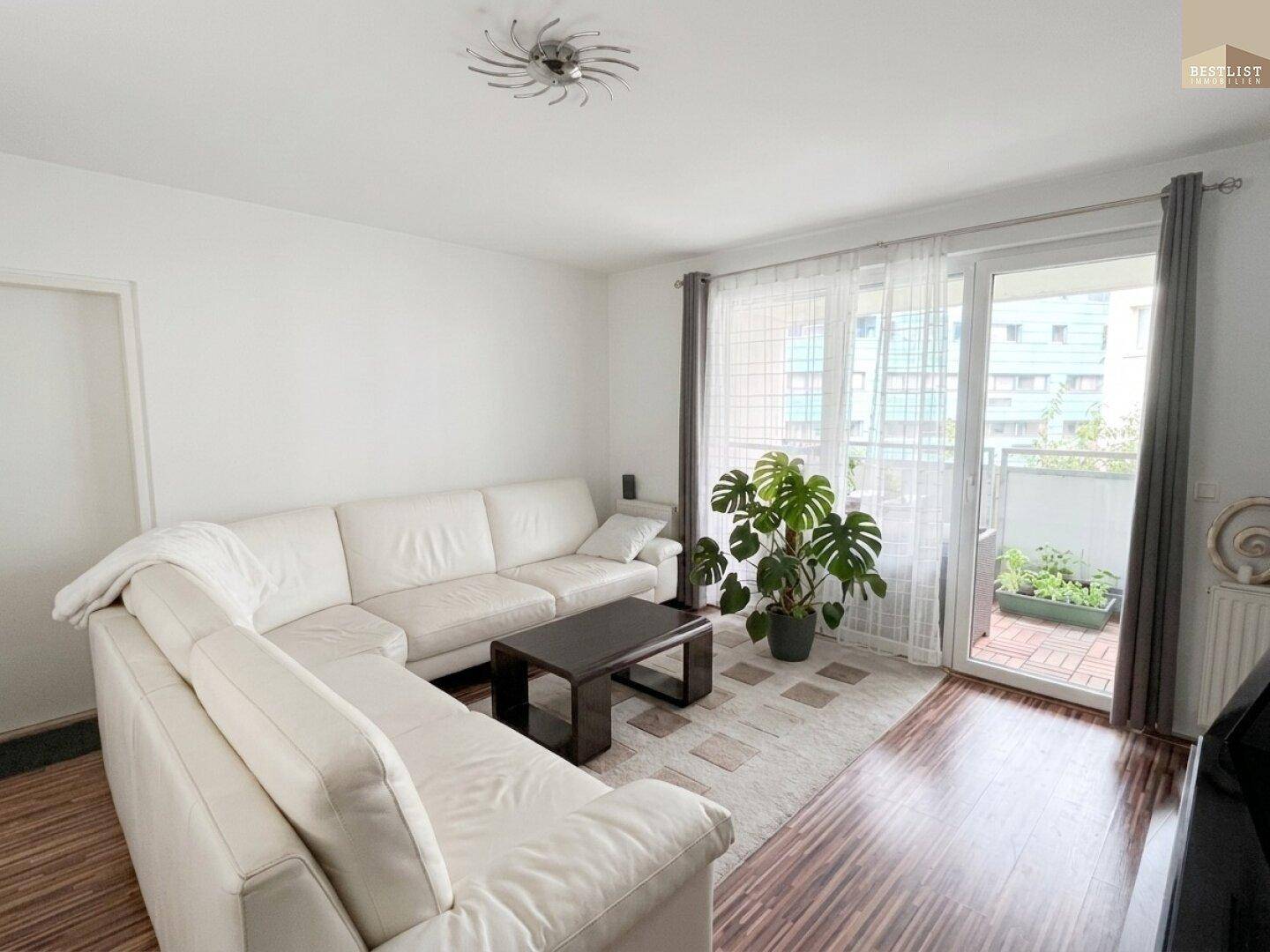 Gemütliches Wohnzimmer mit großem Ecksofa, Holzboden und Zugang zu einem Balkon.