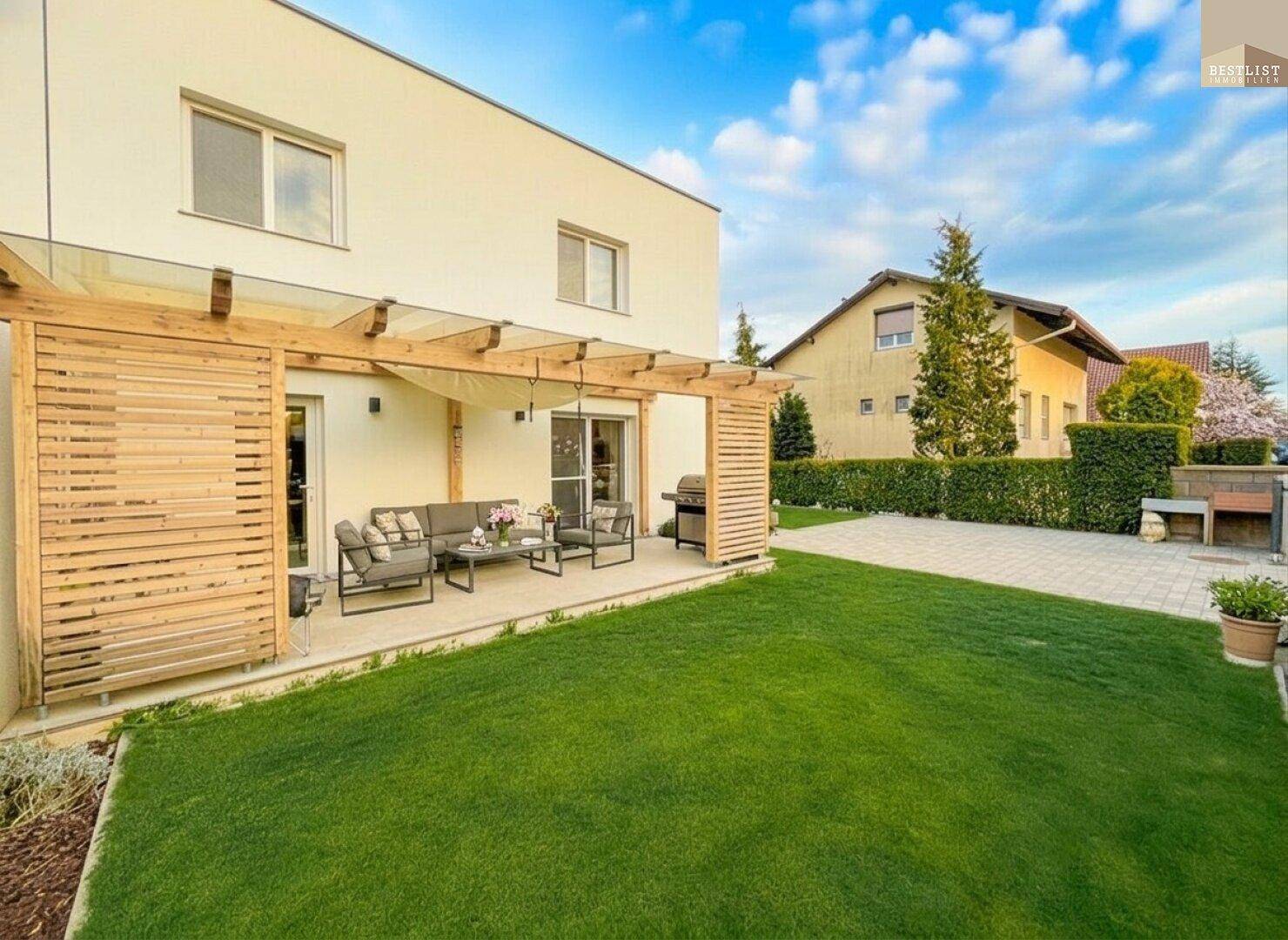 Geräumige Terrasse mit moderner Lounge-Möblierung und Grillbereich, umgeben von einem grünen Garten.
