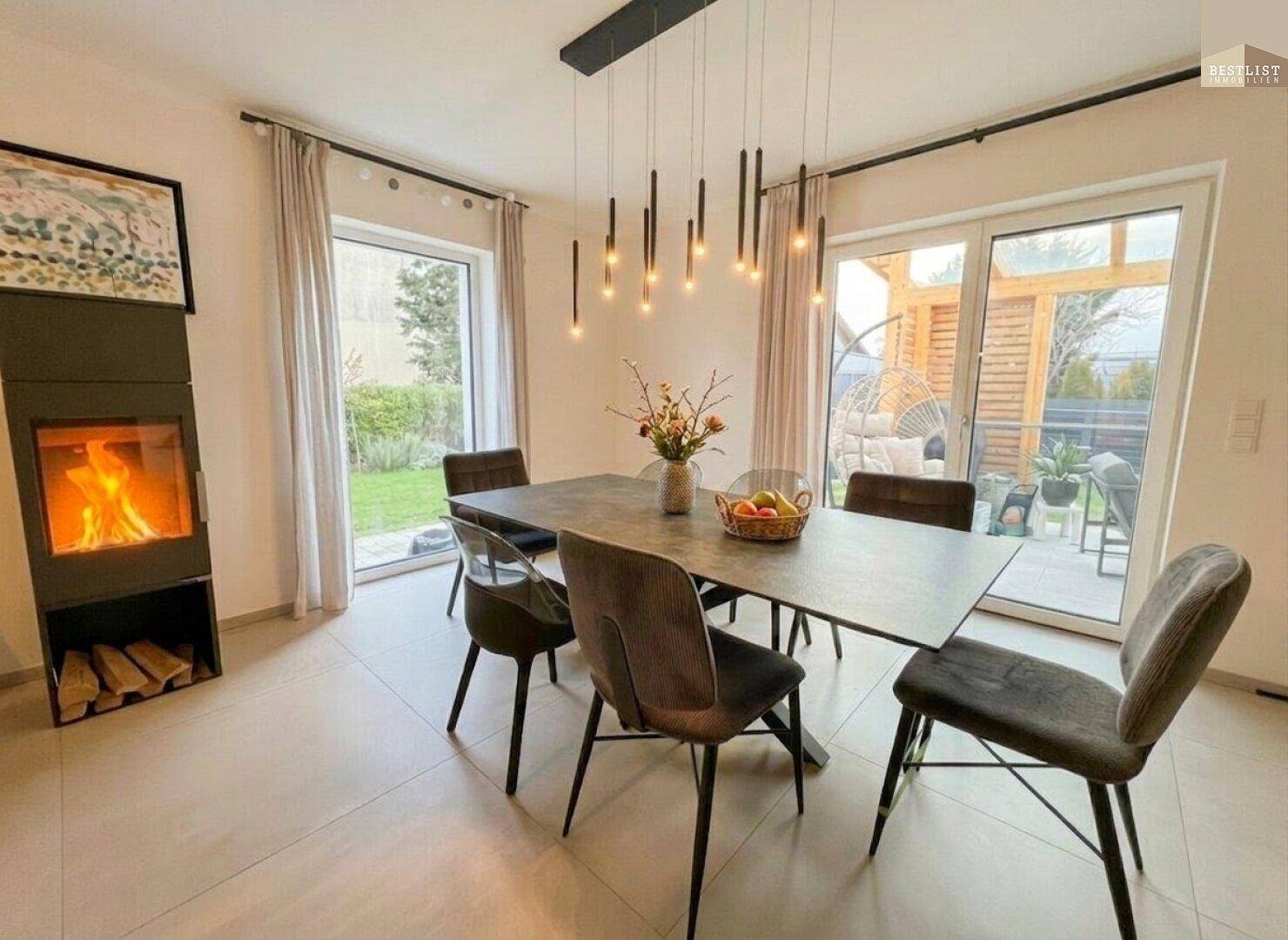 Heller Essbereich mit modernem Kamin, großem Esstisch und Zugang zur Terrasse mit Gartenblick.
