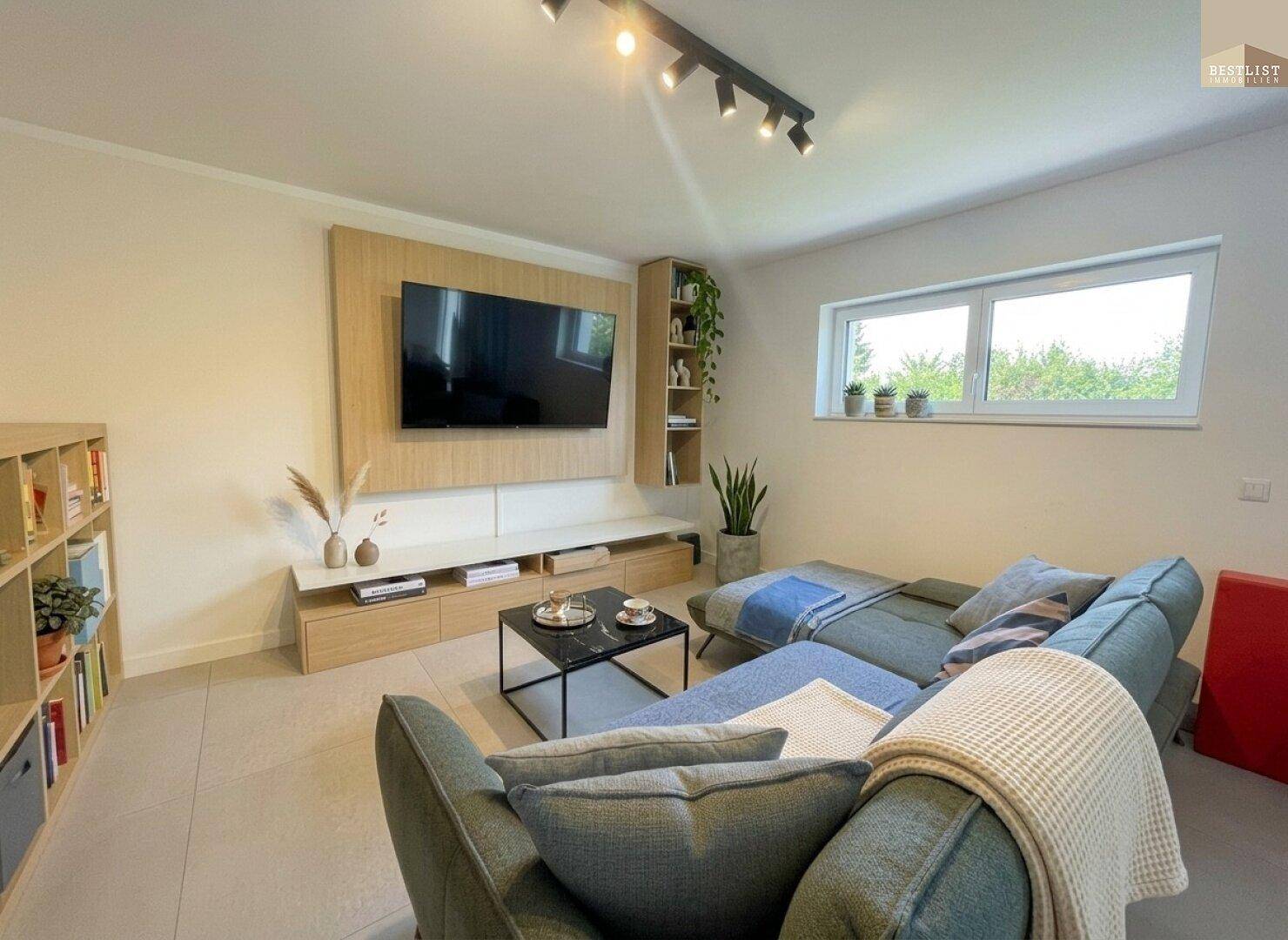 Gemütliches Wohnzimmer mit großem Ecksofa, modernem TV-Möbel und viel natürlichem Licht durch das Fenster.