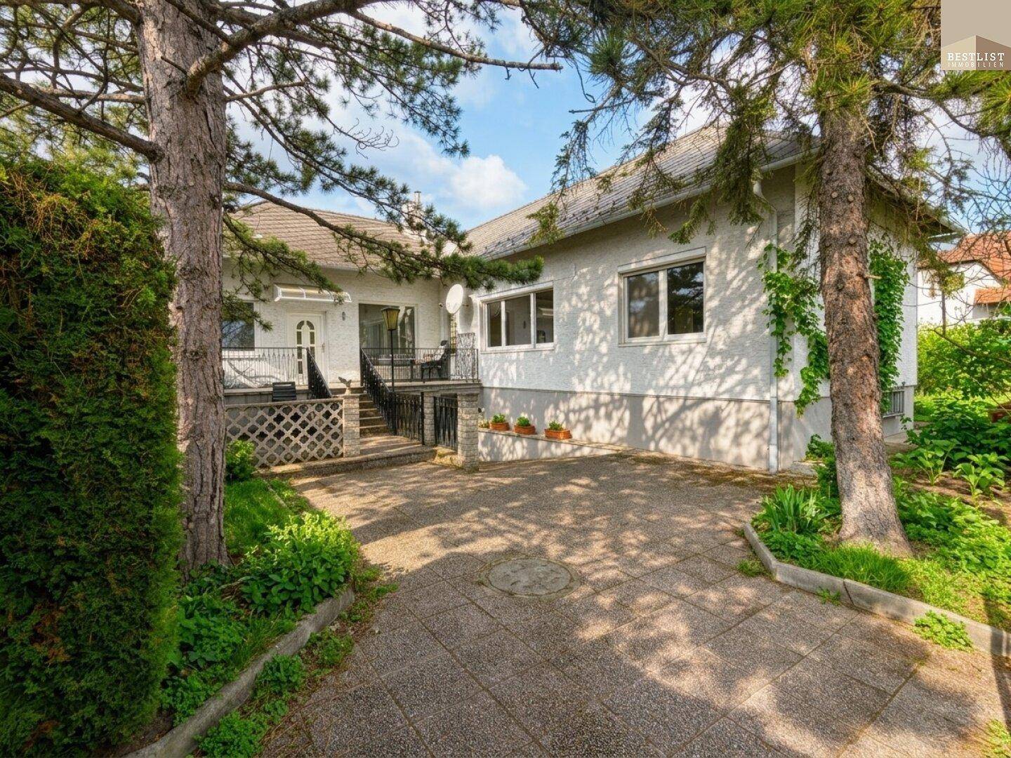Vorderansicht des Hauses mit gepflasterter Einfahrt und umgebenden Bäumen.