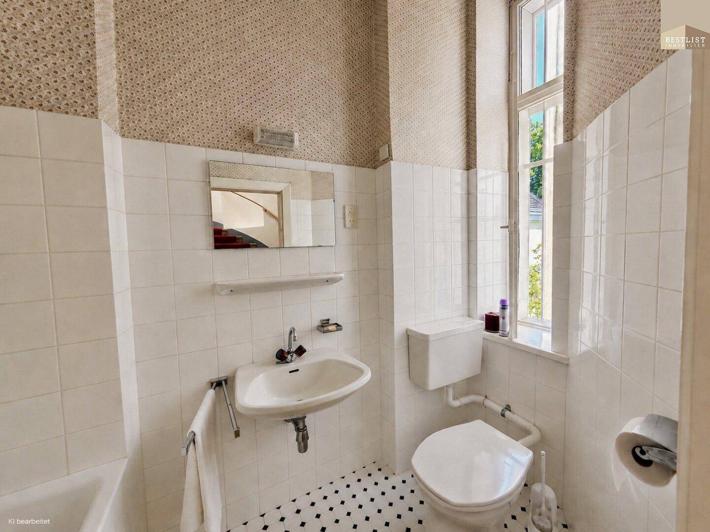 Badezimmer mit weißen Fliesen, gemustertem Boden und einem Fenster für natürliches Licht.