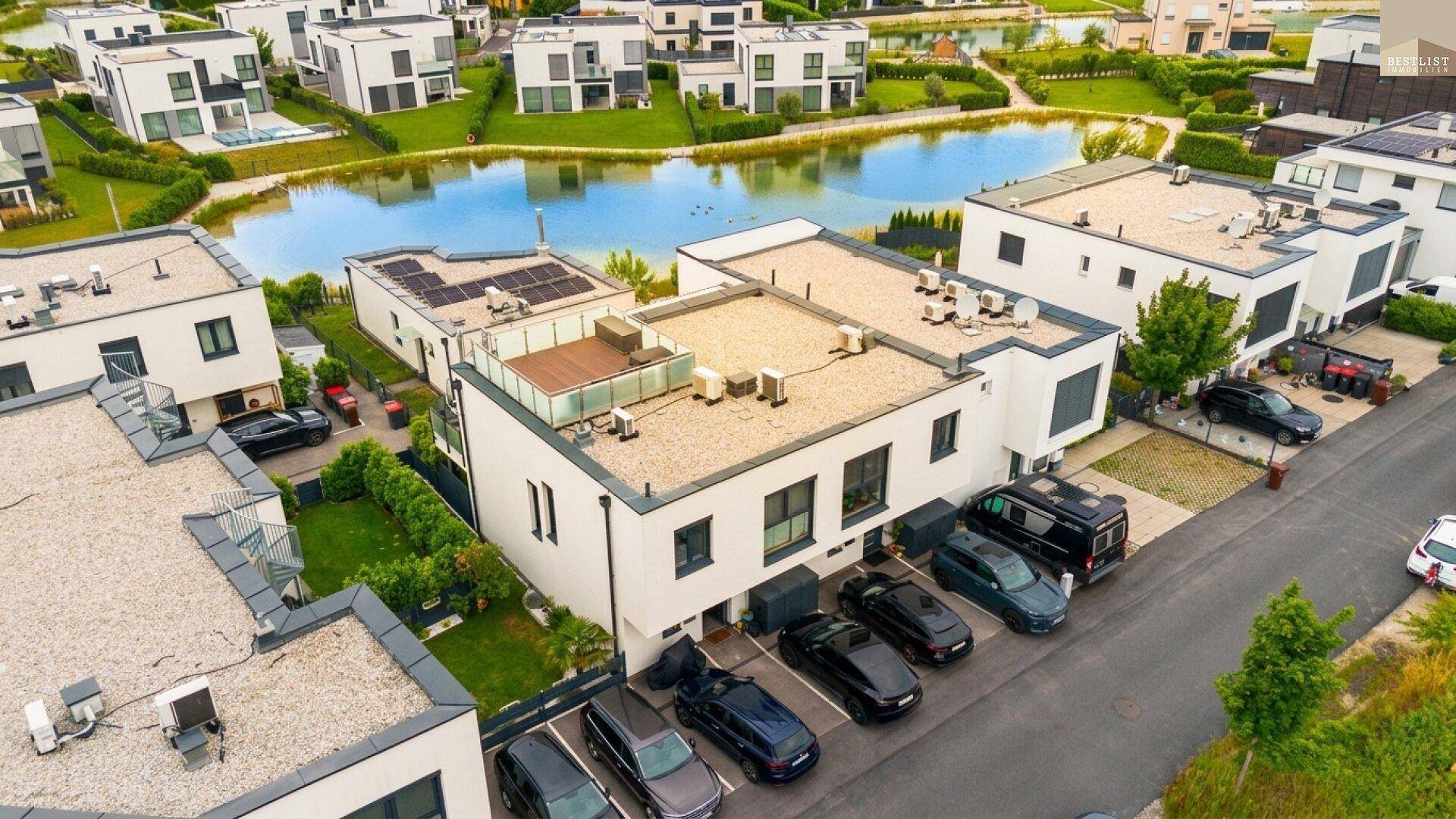 Luftaufnahme einer modernen Wohnsiedlung mit Häusern, See und Parkplätzen.