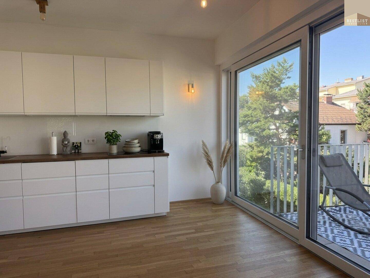 Moderne Einbauküche mit weißen Schränken, Holz-Arbeitsplatte und Zugang zu einem sonnigen Balkon.