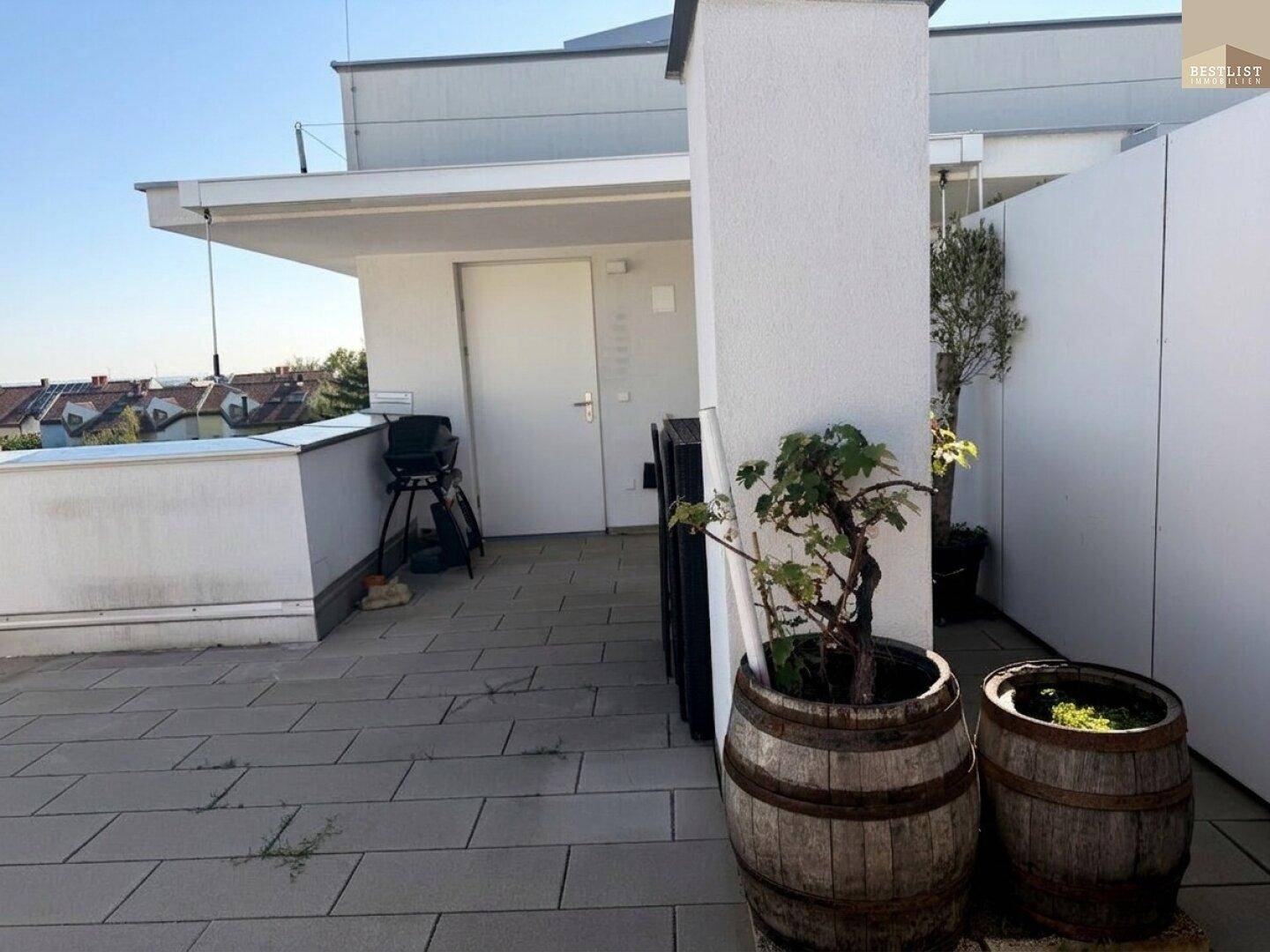 Teil der Dachterrasse mit Fliesenboden, Grill und Zugang zu einem Innenraum.