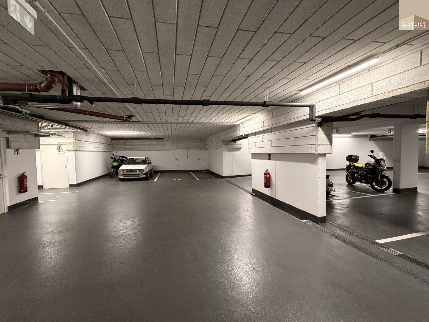 Weitläufige Tiefgarage mit mehreren Stellplätzen für Autos und Motorräder.