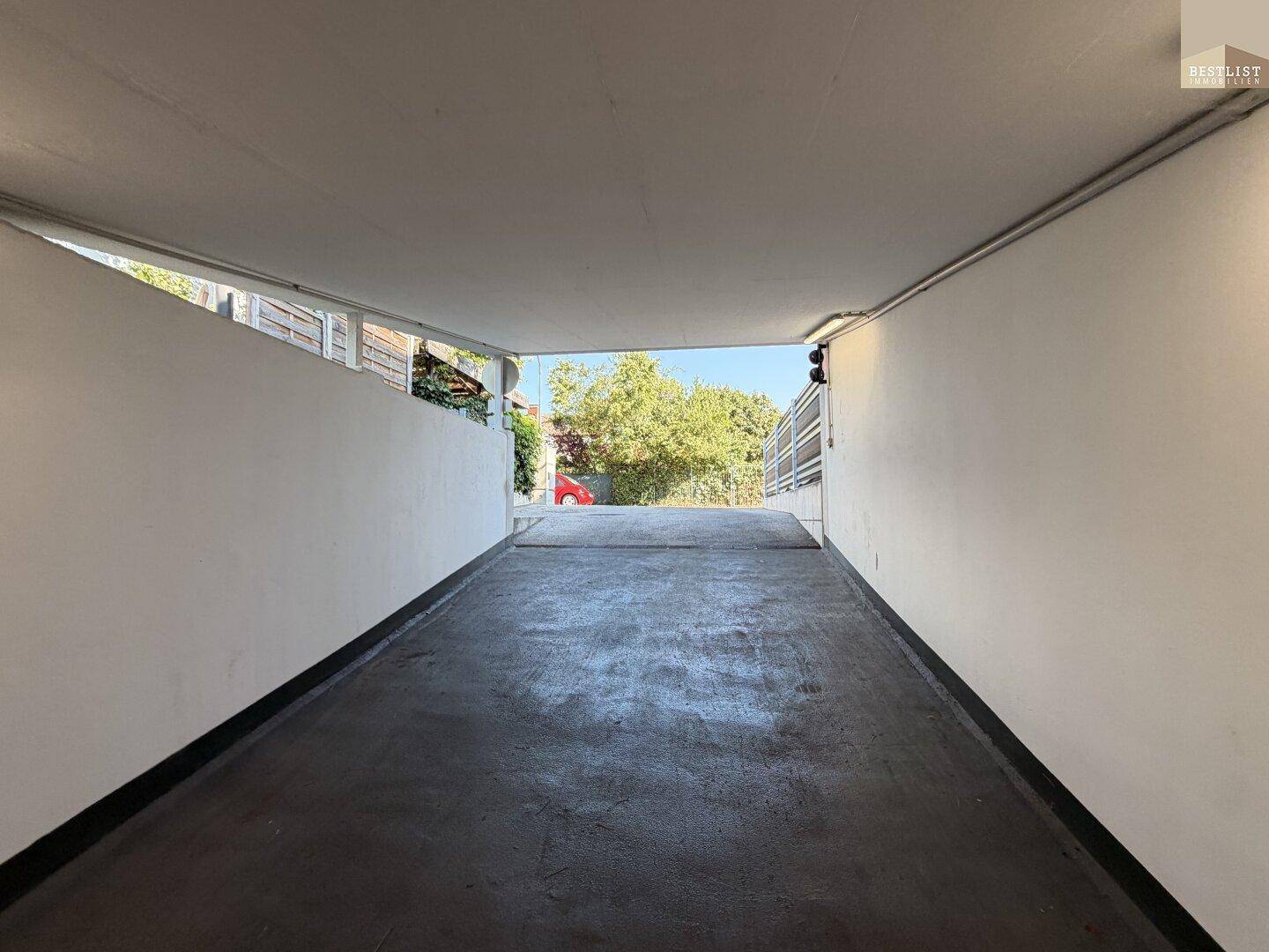 Zufahrtsrampe zur Tiefgarage mit klarem Himmel und umgebendem Grün.