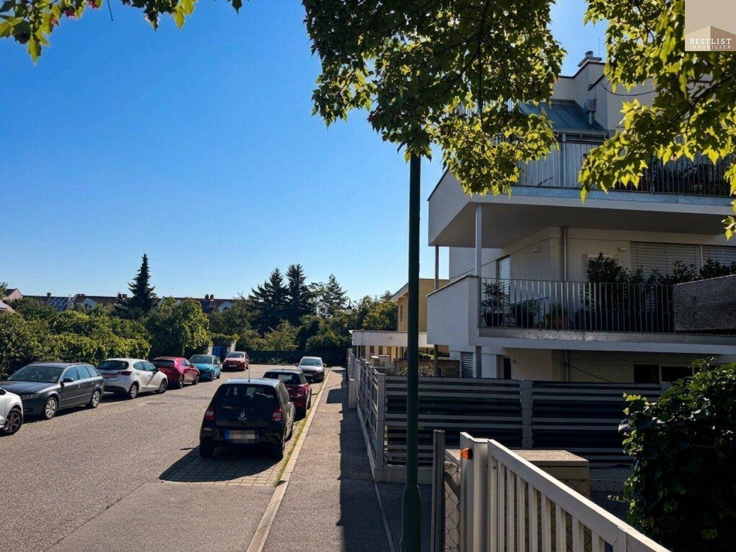 Ruhige Wohnstraße mit parkenden Autos und dem modernen Mehrfamilienhaus im Hintergrund.