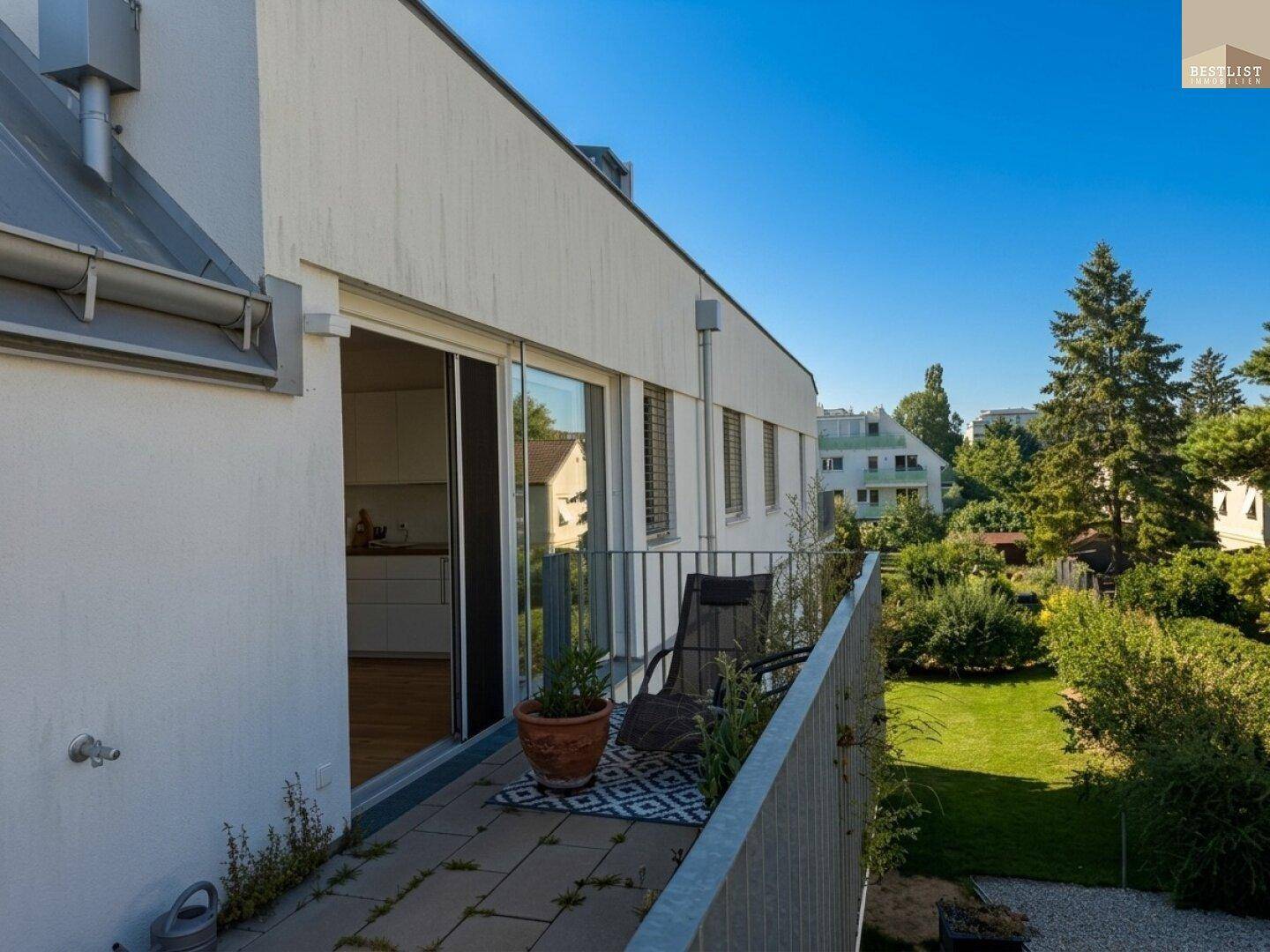 Sonniger Balkon mit Fliesenboden, Sitzgelegenheit und Blick auf den grünen Gartenbereich.
