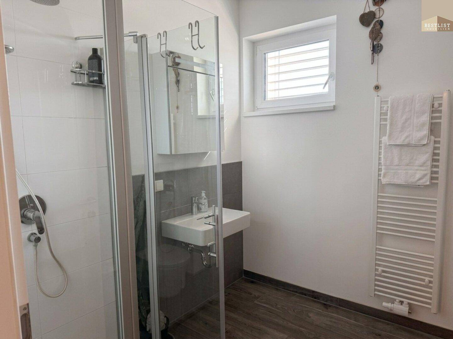Modernes Badezimmer mit Duschkabine, Waschbecken, beheiztem Handtuchhalter und Fenster.