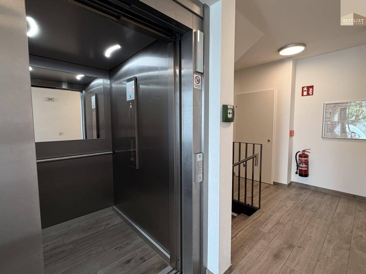 Moderner Aufzug im Eingangsbereich des Gebäudes mit Edelstahloberflächen und Fliesenboden.