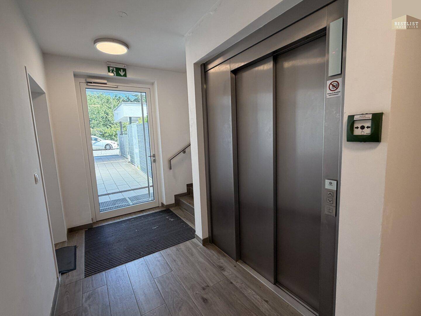 Heller Eingangsbereich mit Aufzug, Zugang zum Freien und Fliesenboden.