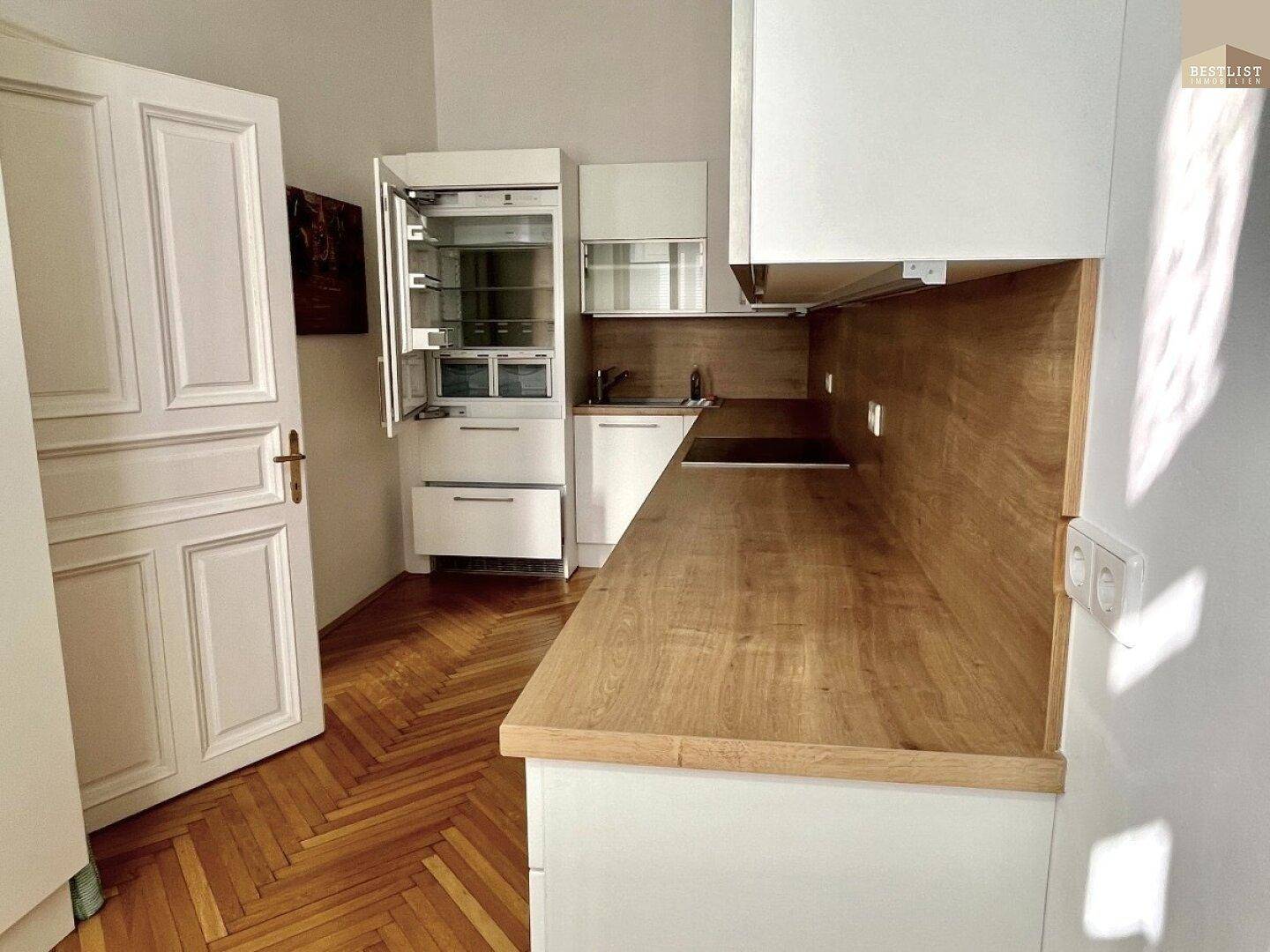 Kompakte Küche mit integriertem Kühlschrank, Holz-Arbeitsplatte und weißen Schränken.