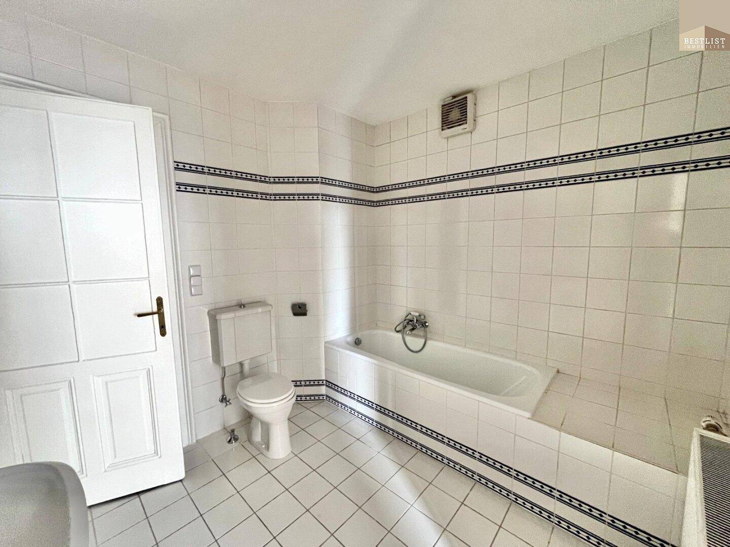 Klassisches Badezimmer mit Badewanne, WC und weißen Fliesen mit dekorativer Bordüre.
