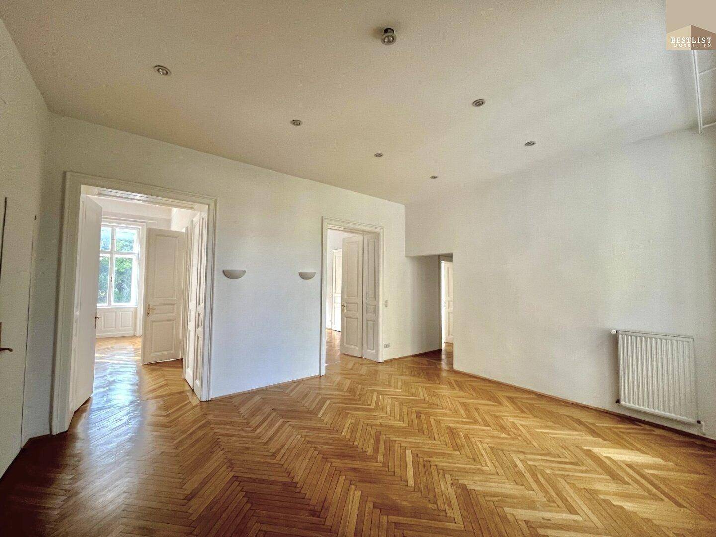Großer Wohnraum mit Fischgrätparkett, hohen Decken und integrierter Deckenbeleuchtung für eine angenehme Atmosphäre.