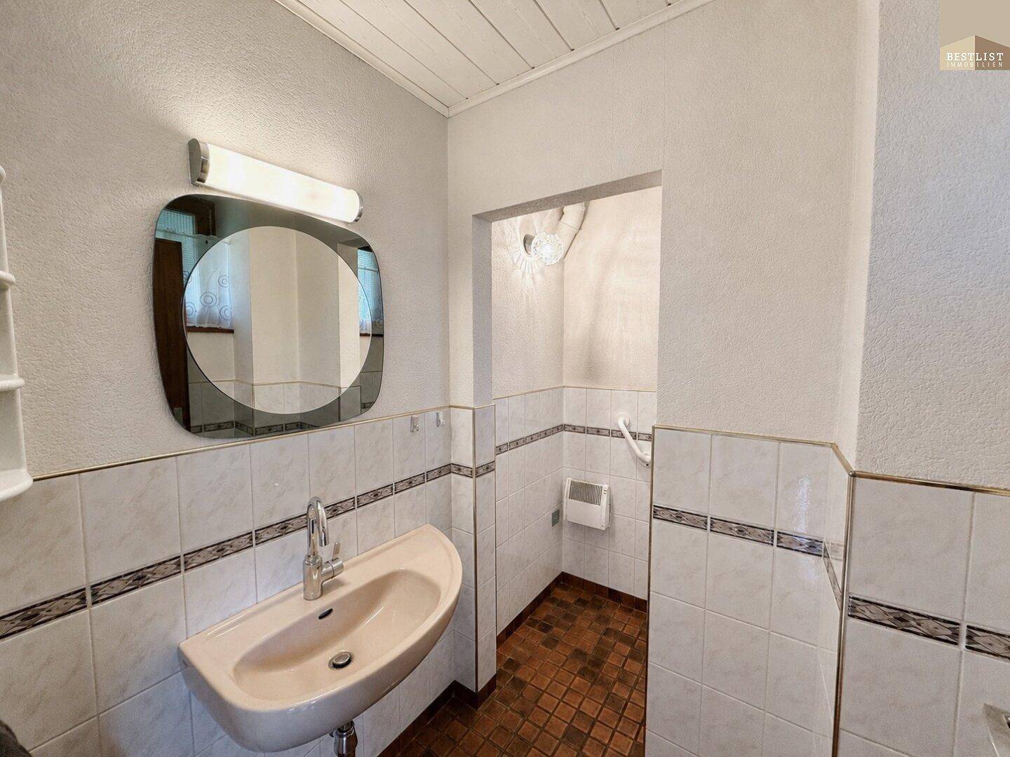 Kleines Gäste-WC mit Waschbecken und hellen Fliesen an den Wänden.
