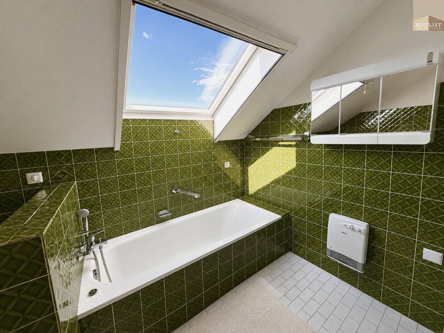 Badezimmer mit Badewanne, grünen Fliesen und Dachfenster für viel Tageslicht.