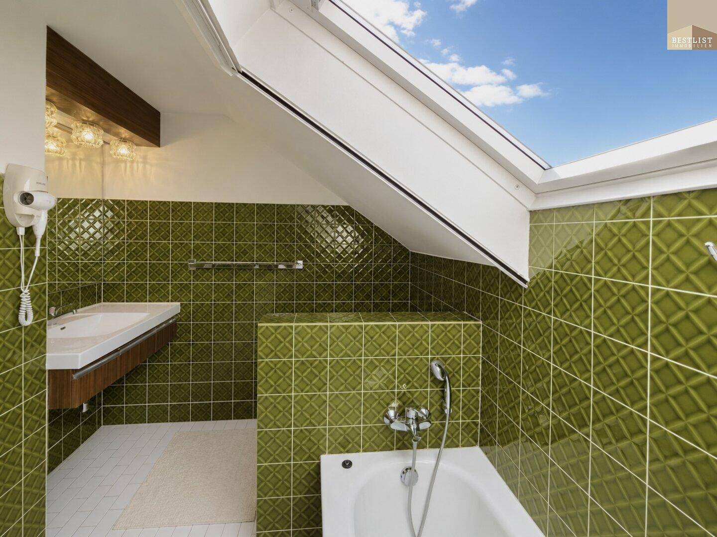 Badezimmer mit Waschbecken, grünen Fliesen und großem Dachfenster.