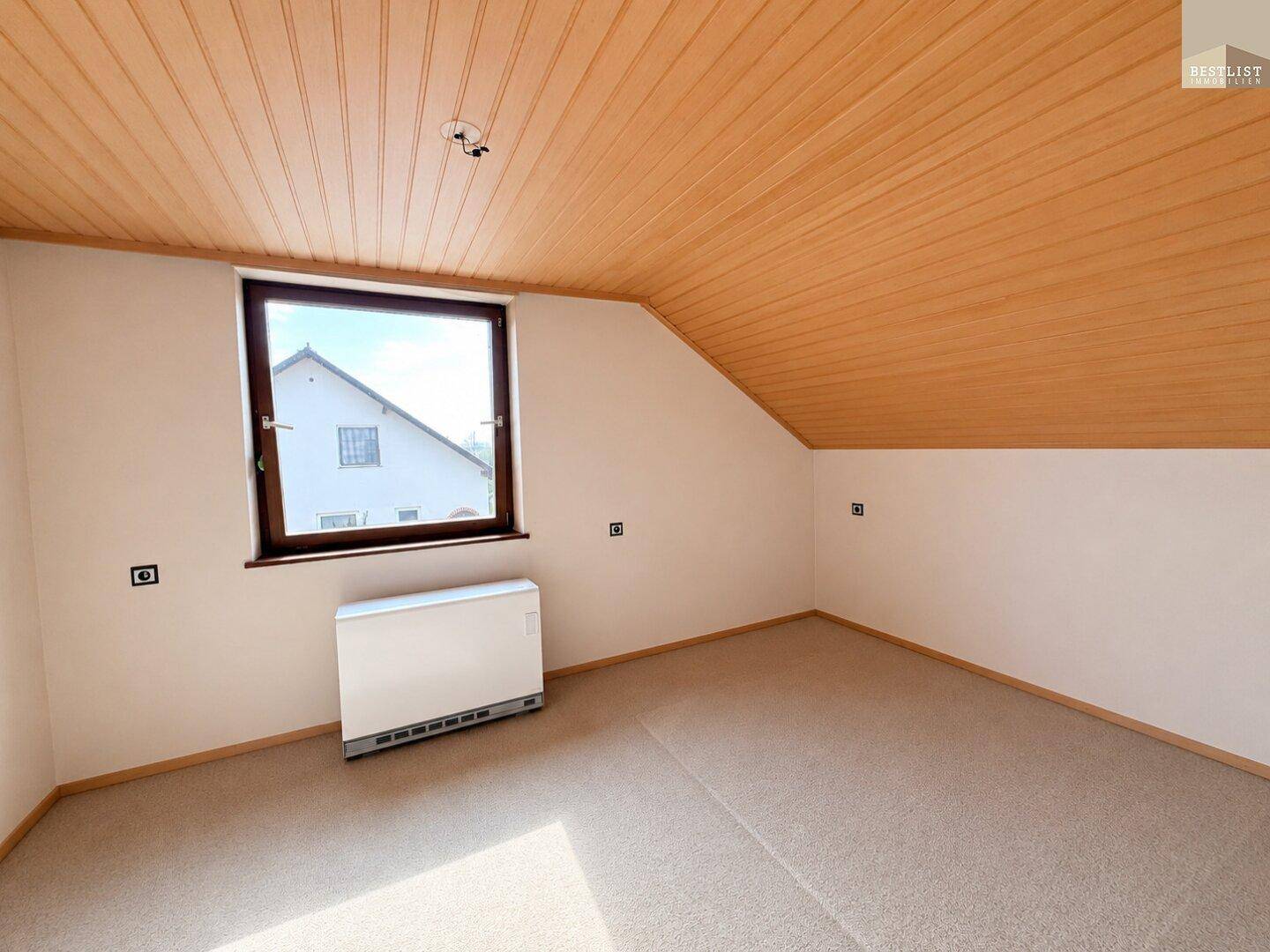 Helles Schlafzimmer im Dachgeschoss mit Teppichboden und Fenster.