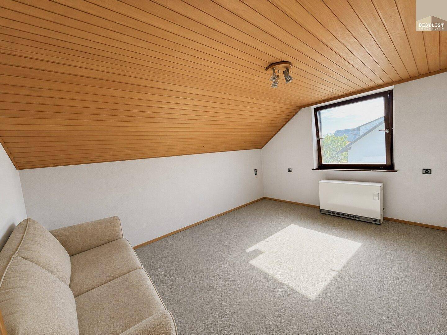 Gemütliches Schlafzimmer im Dachgeschoss mit Teppichboden und Holzdecke.