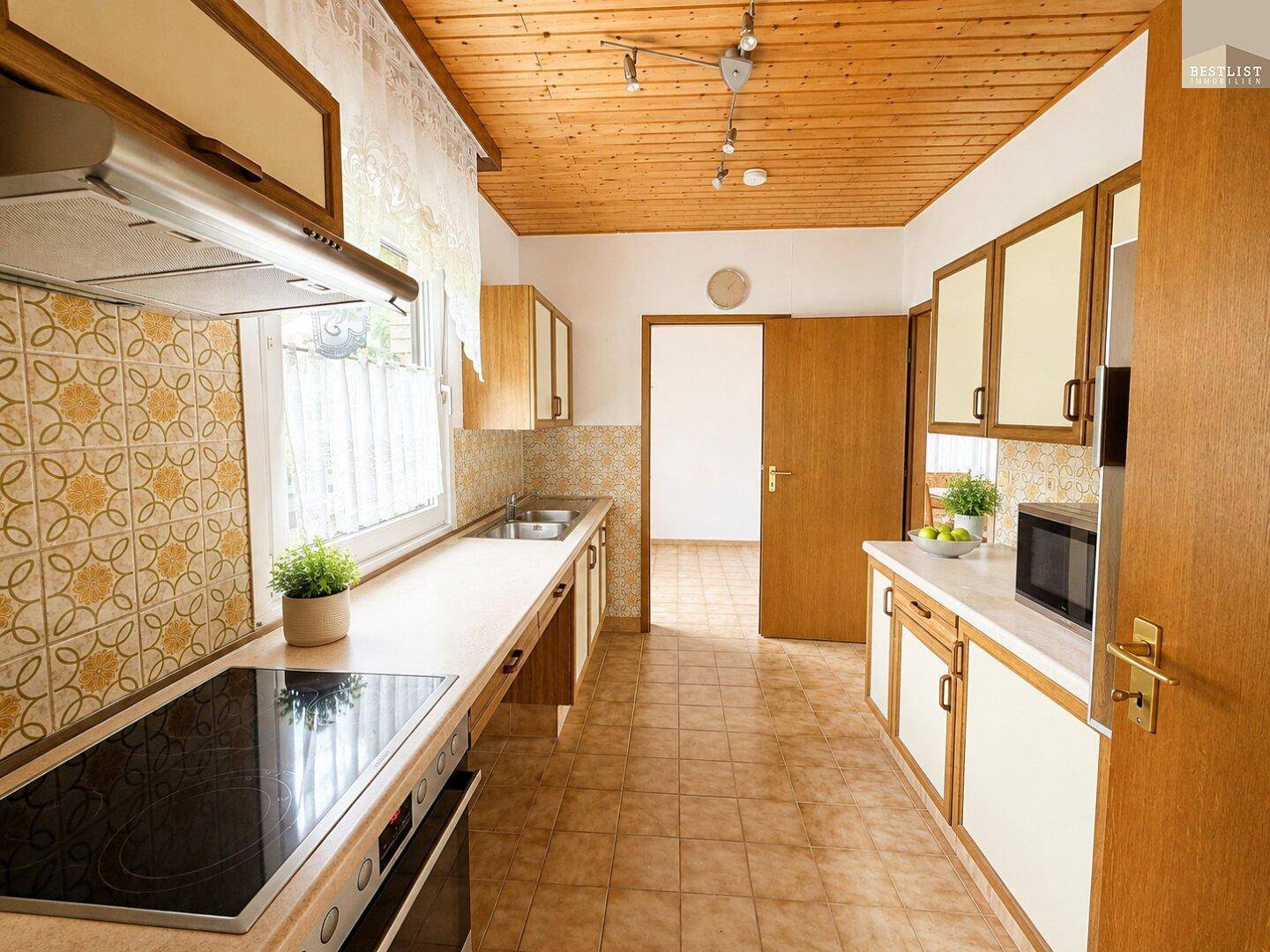 Traditionelle Küche mit Holzschränken, Fliesenboden und einem Fenster über der Spüle.