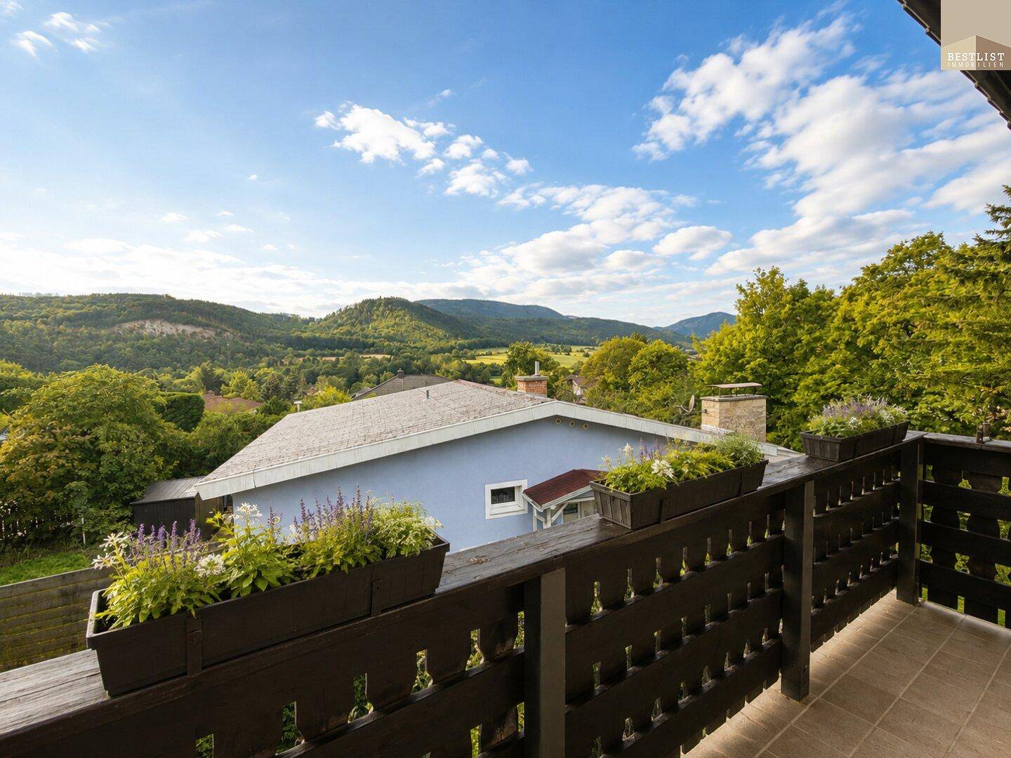 Balkon mit Blumenkästen und weitem Blick auf die umliegende grüne Hügellandschaft.
