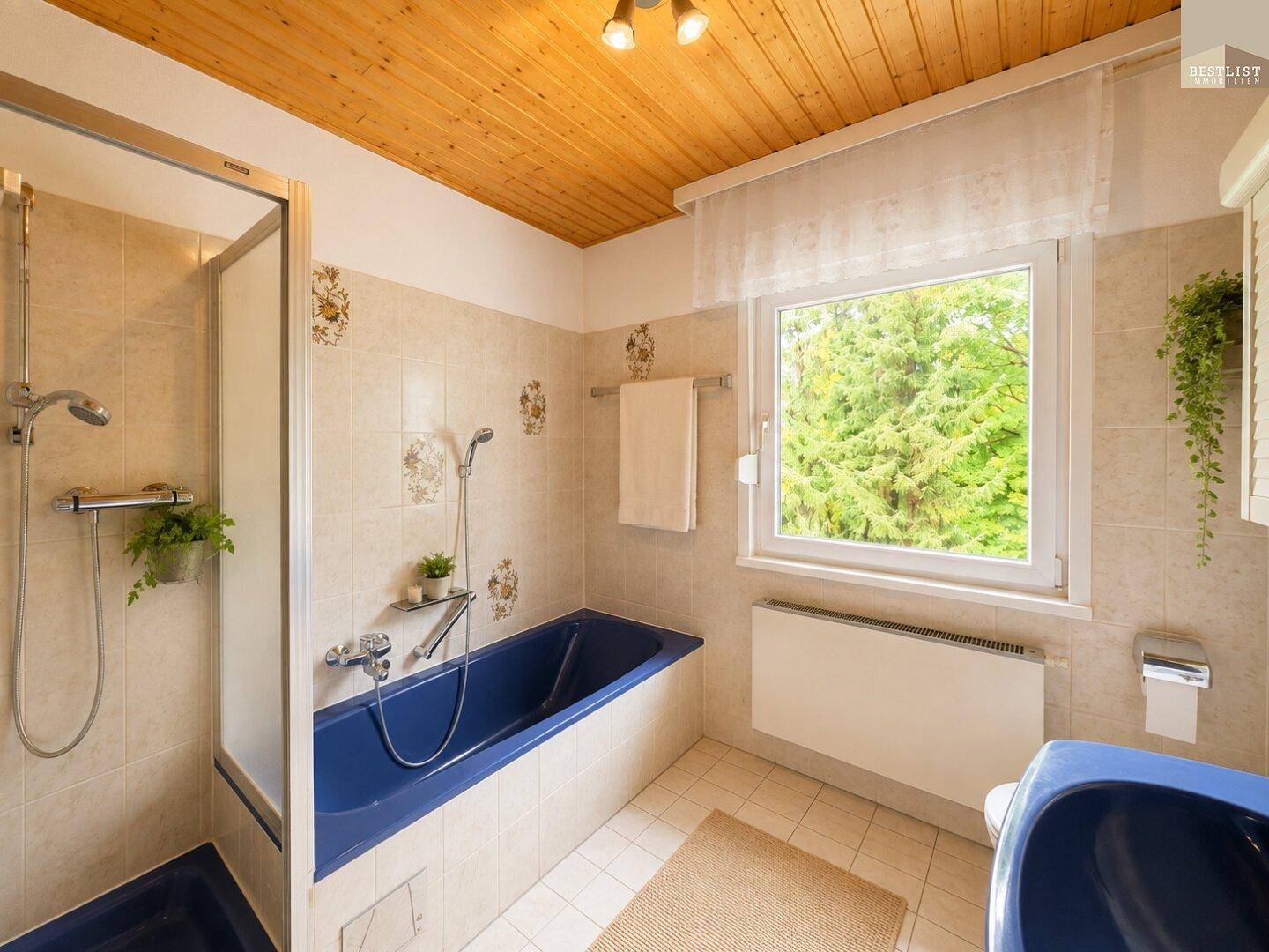 Badezimmer im Stil der 80er Jahre mit blauer Badewanne, Dusche und Fenster.