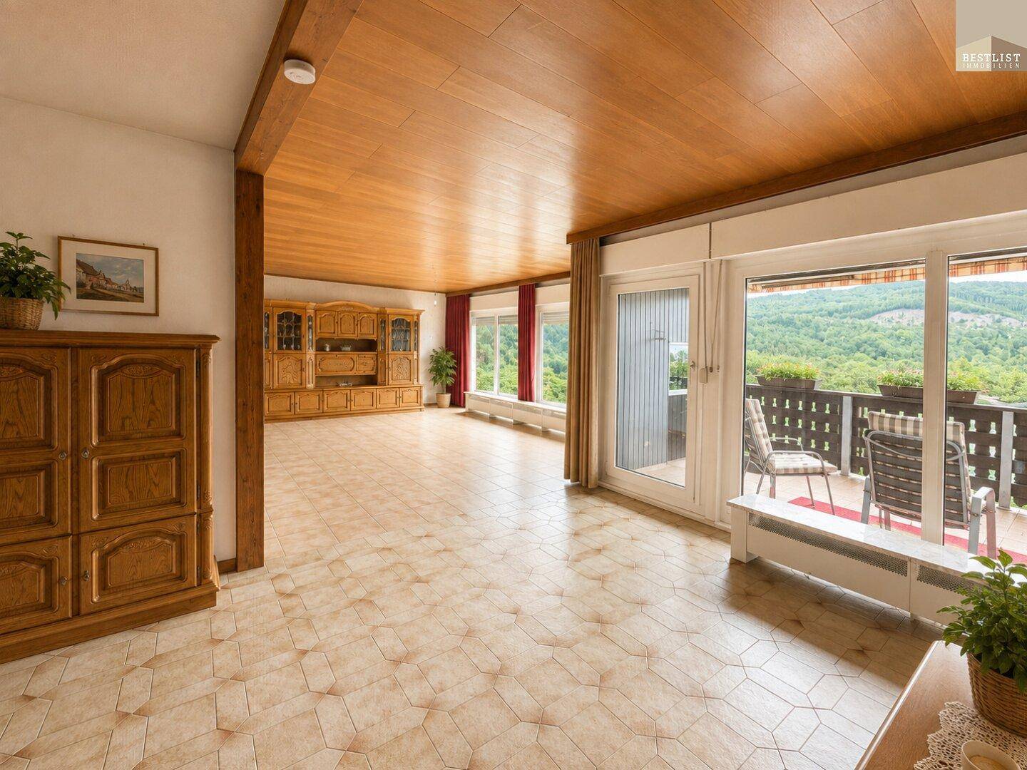 Geräumiges Wohnzimmer mit Holzbalken, Holzdecke und Zugang zu einem Balkon mit Aussicht.