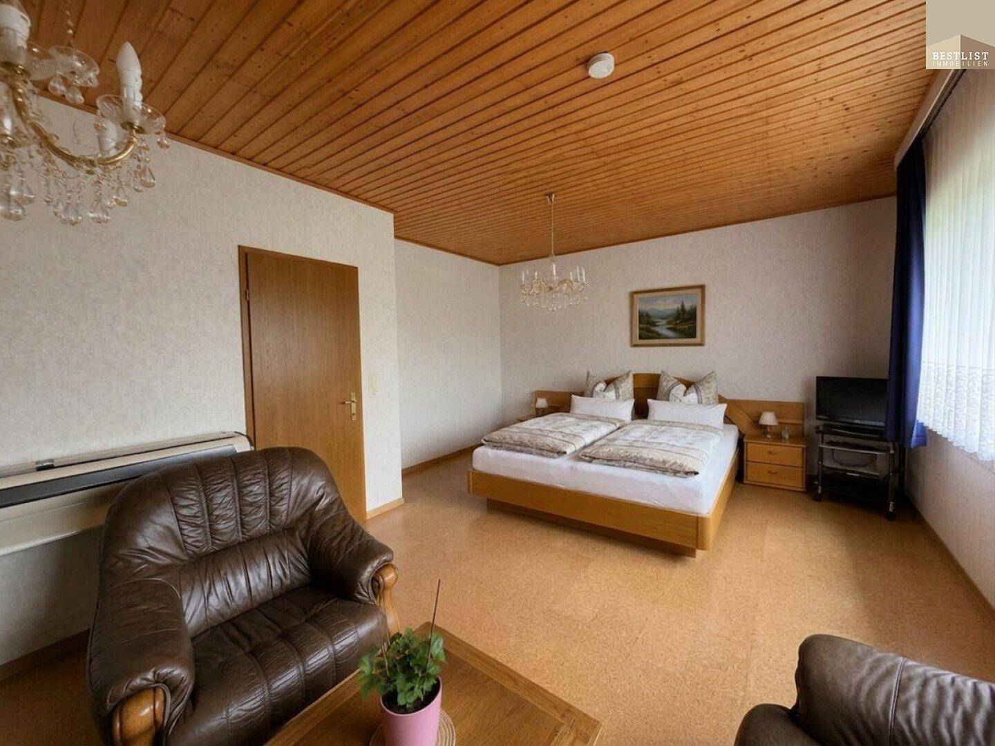 Geräumiges Schlafzimmer mit Doppelbett, Holzdecke und Ledersesseln, ausgestattet mit Kronleuchter.