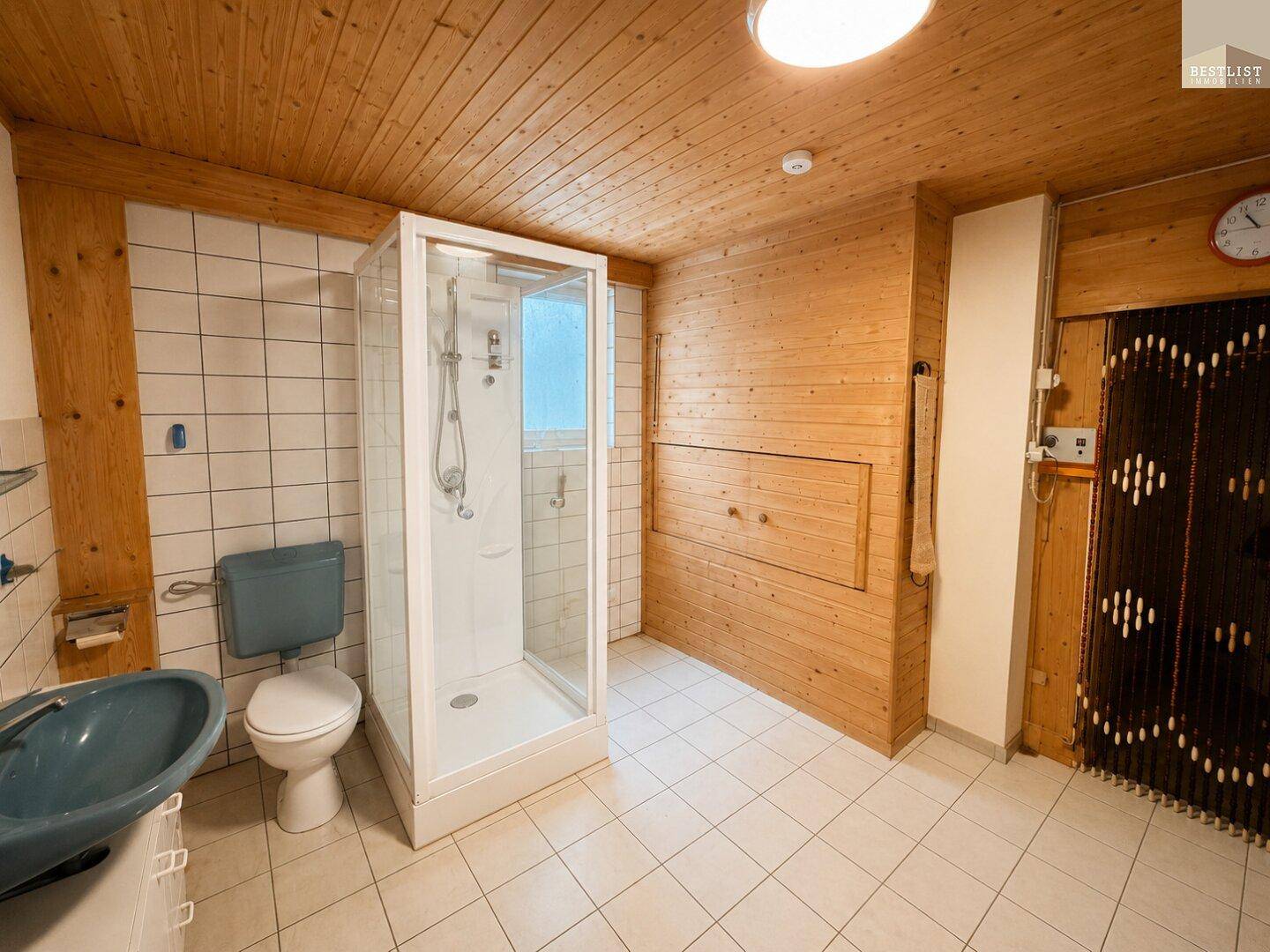 Rustikales Badezimmer mit Holzverkleidung, Duschkabine und WC, im Kellerbereich gelegen.