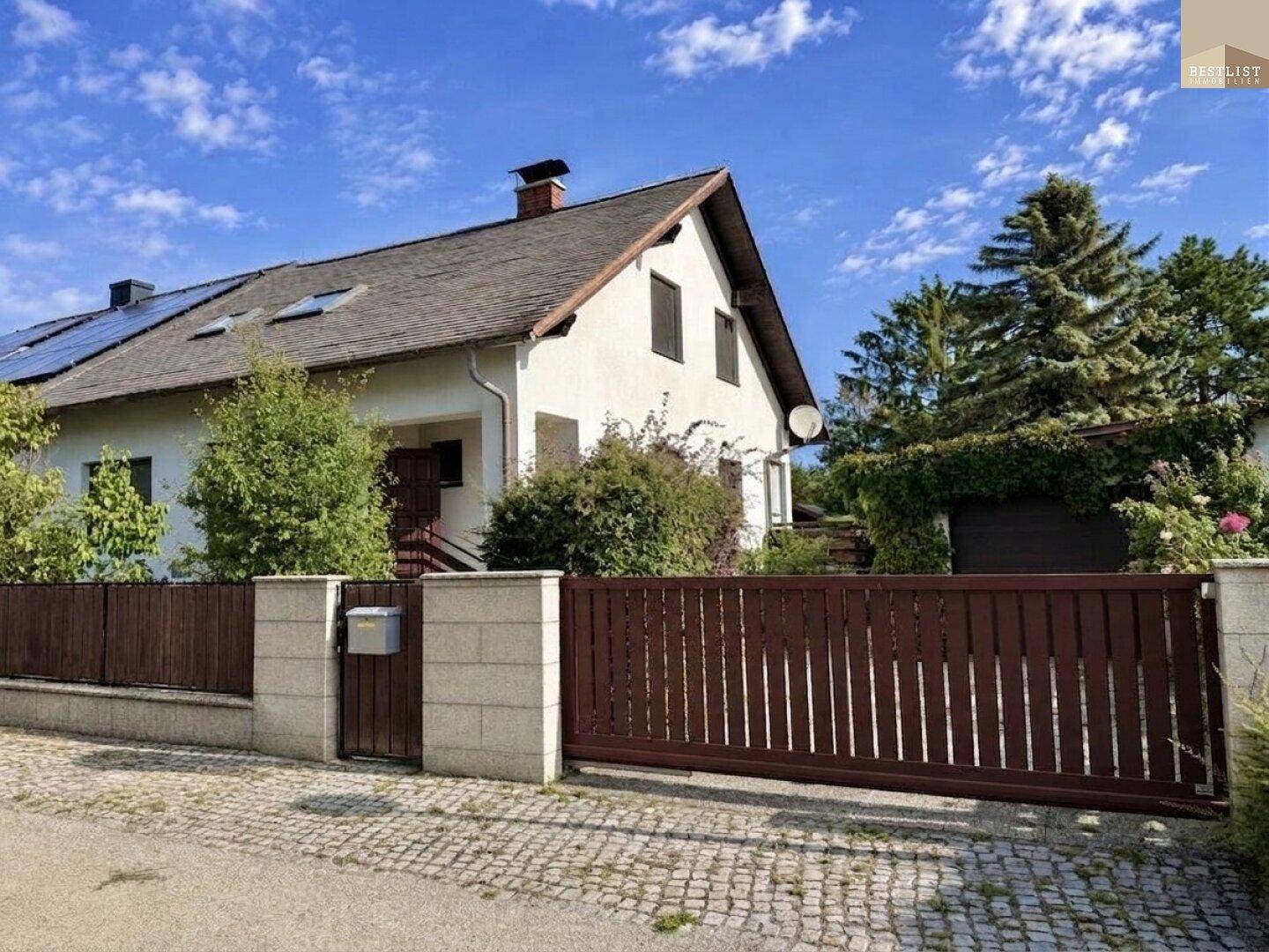 Ansicht des Hauses von der Straße mit Zaun und Photovoltaikanlage auf dem Dach.